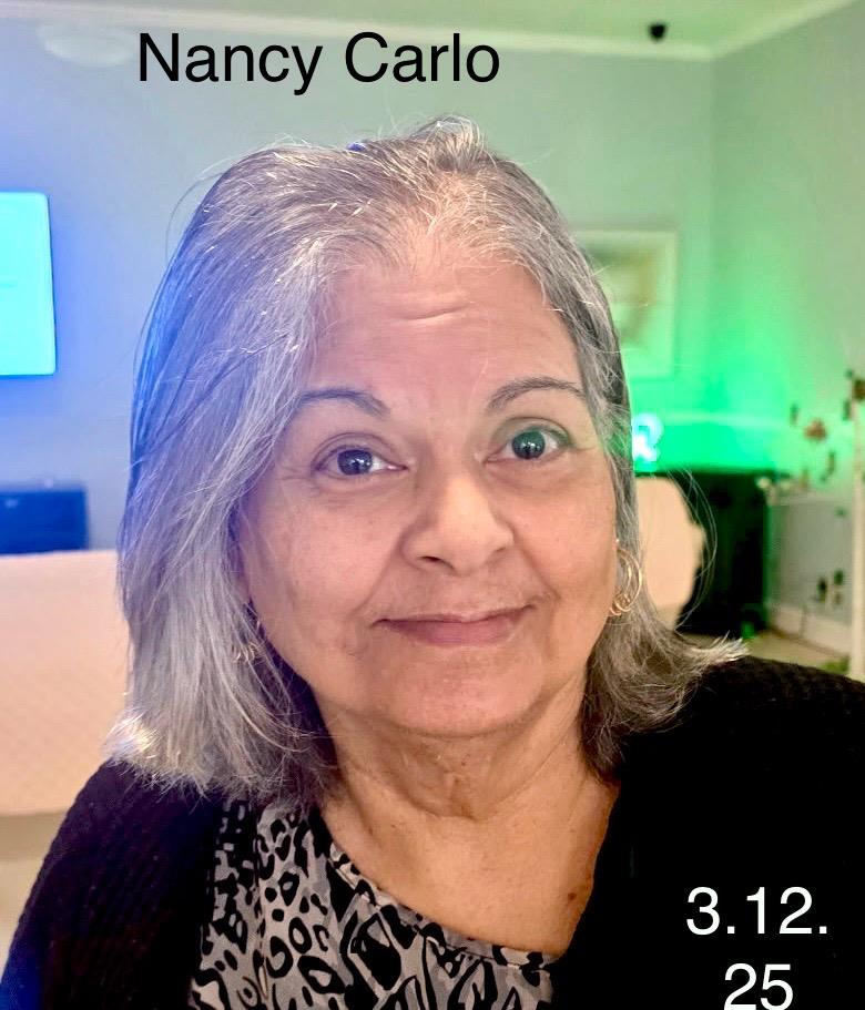 Older woman with silver hair and glasses smiles warmly in a stylish, brightly lit room.