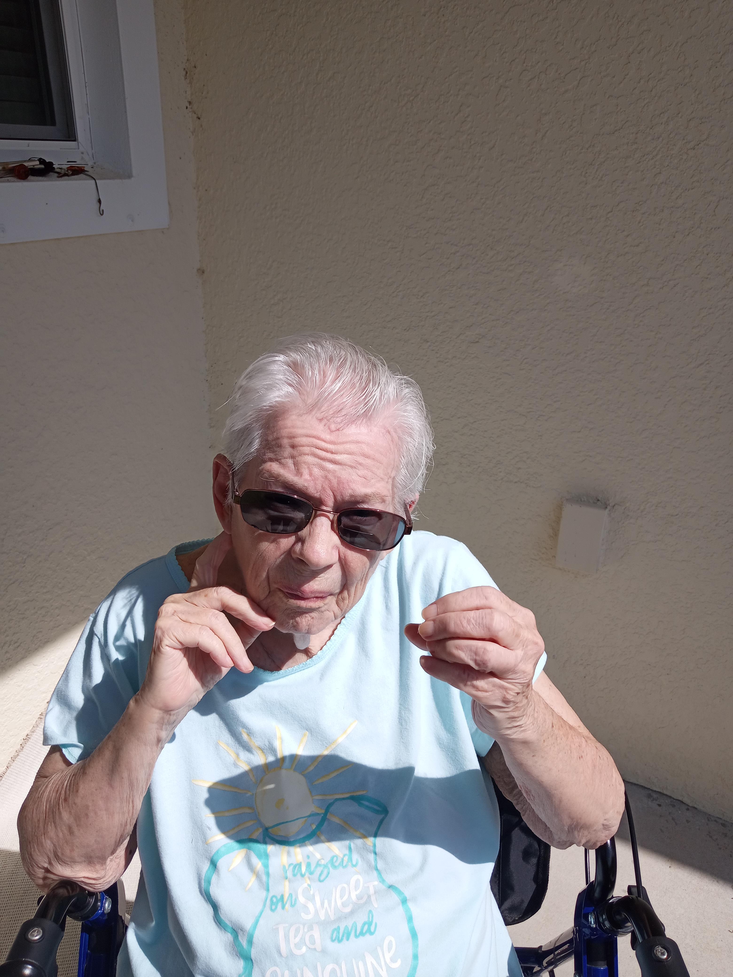 An elderly man in sunglasses sits outdoors, contemplative with an object in hand.