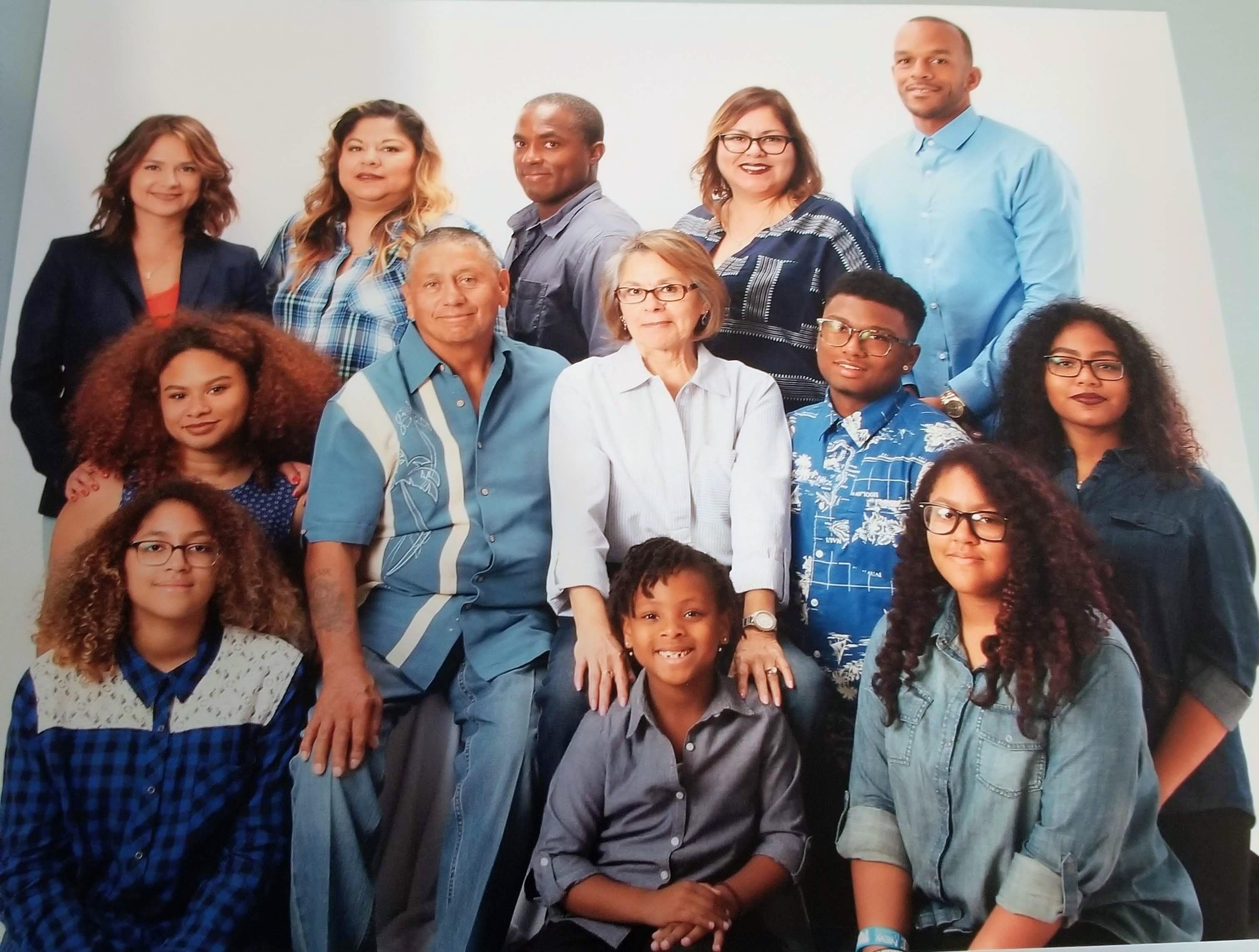 A diverse group of family members poses together in matching casual outfits, smiling joyfully.