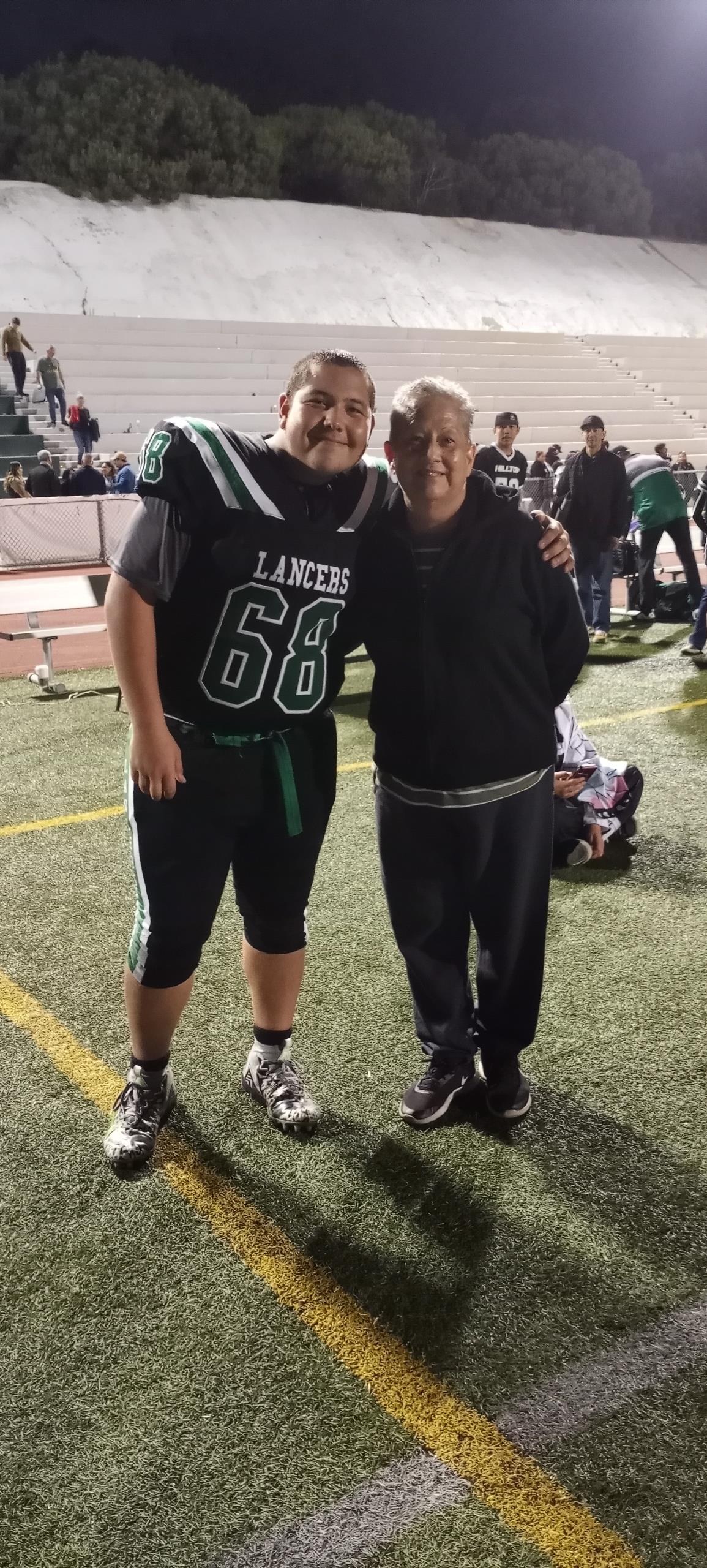 A young football player, wearing jersey number 68, poses with his coach on the field at night.