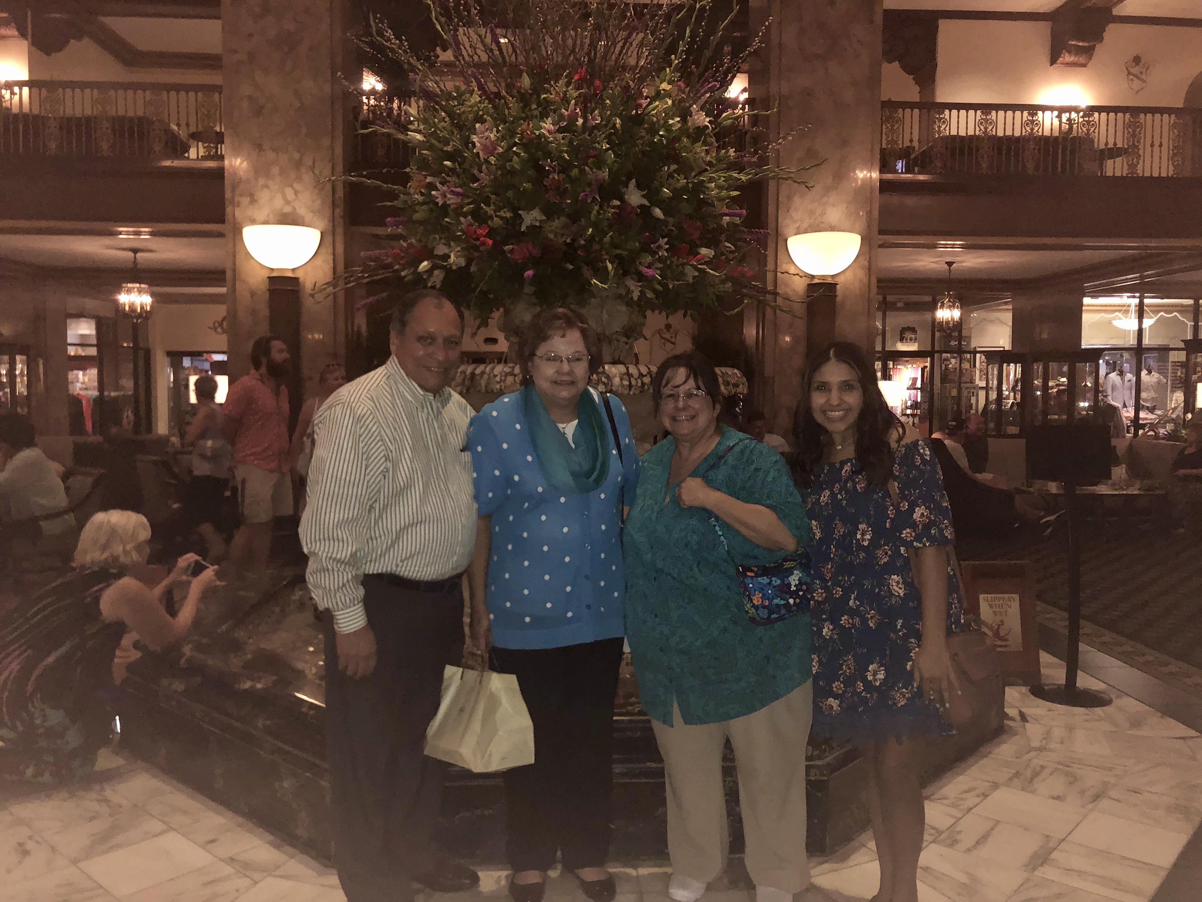 Four friends smile together in a hotel lobby near a large floral display.