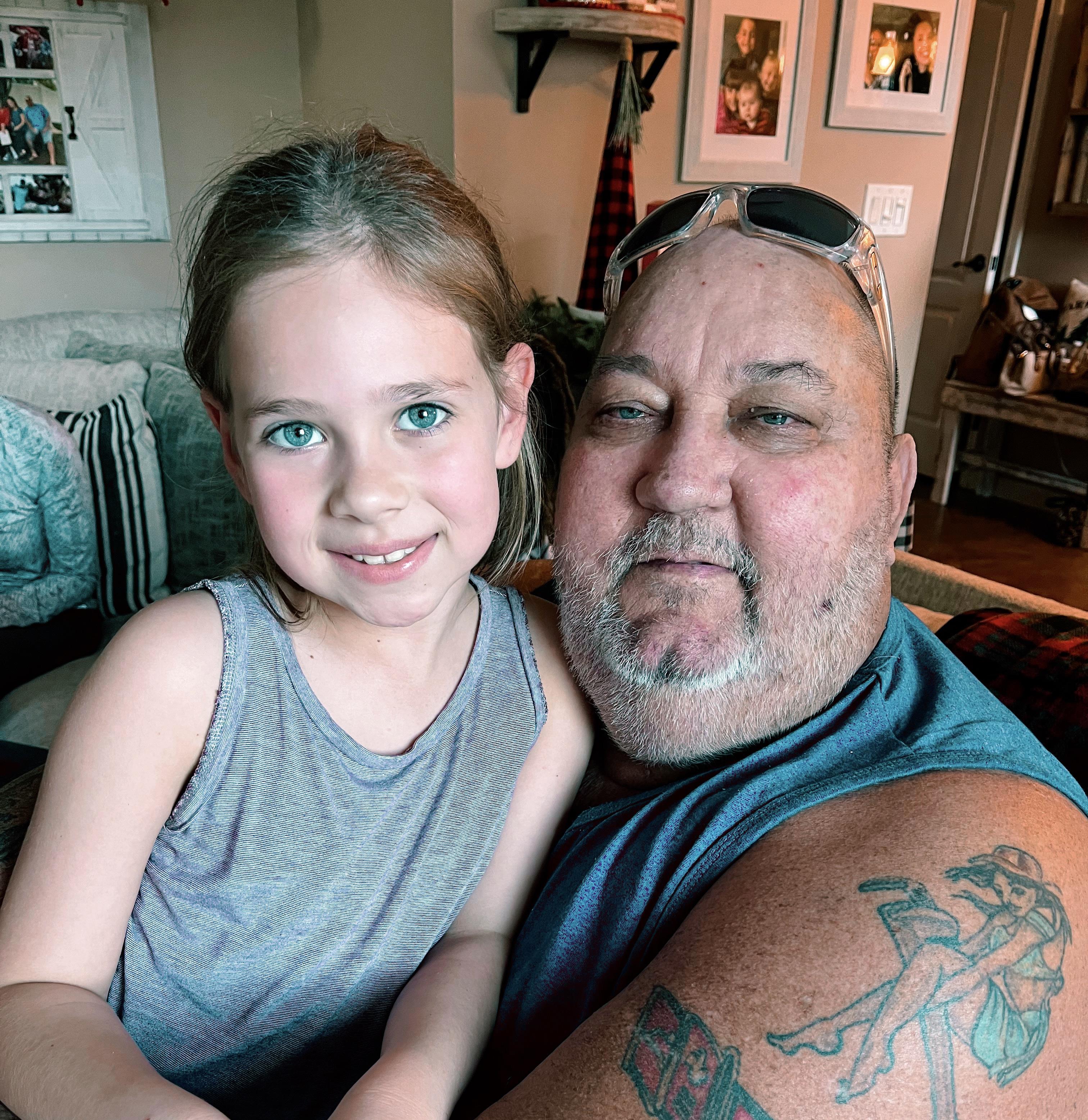 A grandfather and his granddaughter smile together while enjoying quality time indoors.