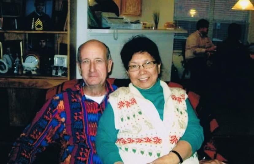 Two individuals sit closely together, smiling warmly in a comfortable home setting during winter.