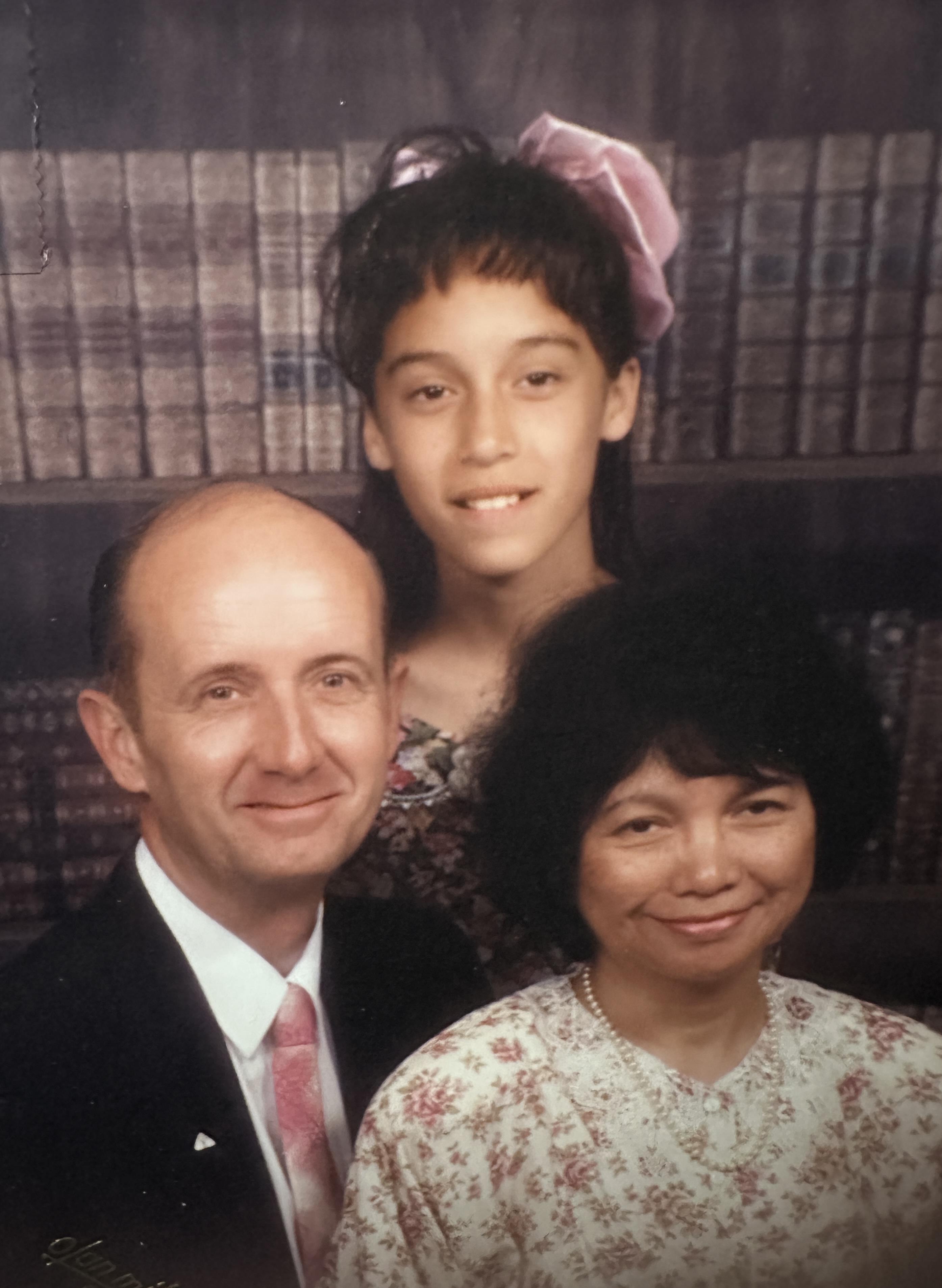 A smiling family poses together in a warmly lit indoor area, surrounded by books.