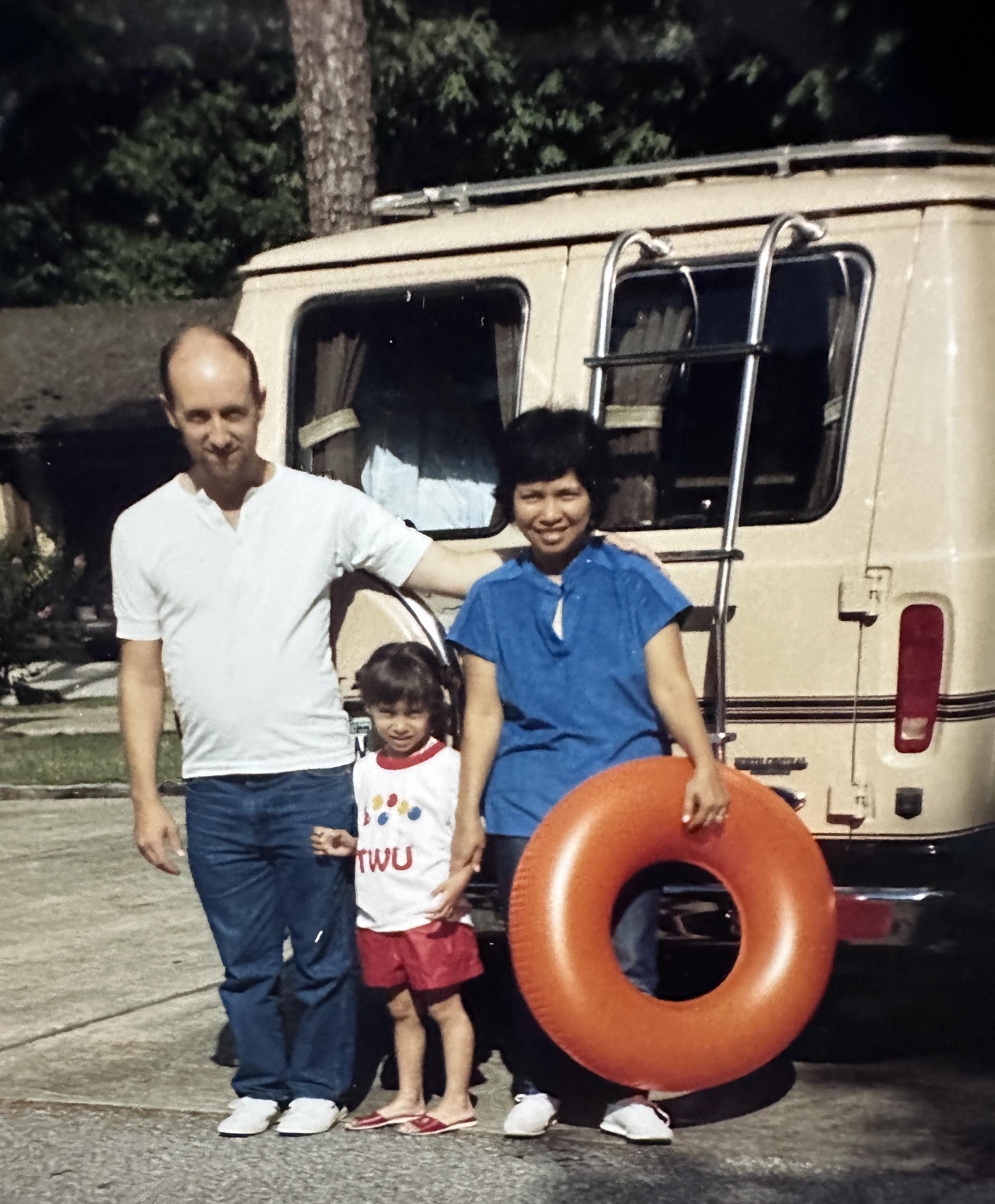 A family stands together outside a van, with a child holding a flotation ring and smiling.