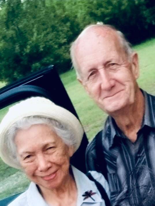Two seniors enjoy their time outdoors smiling happily in a lush park filled with greenery.