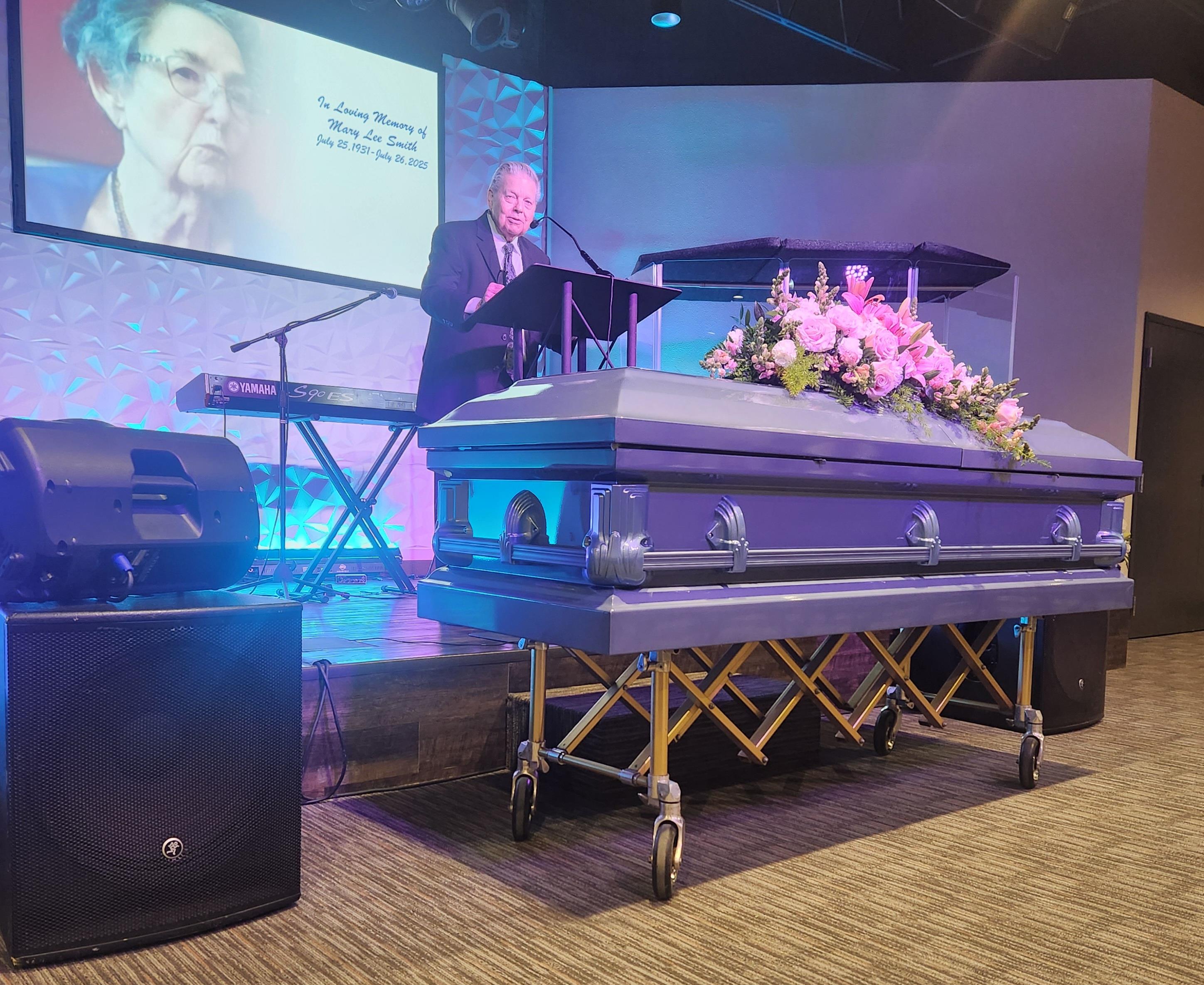 A solemn ceremony takes place as a speaker delivers a eulogy beside a decorated casket.