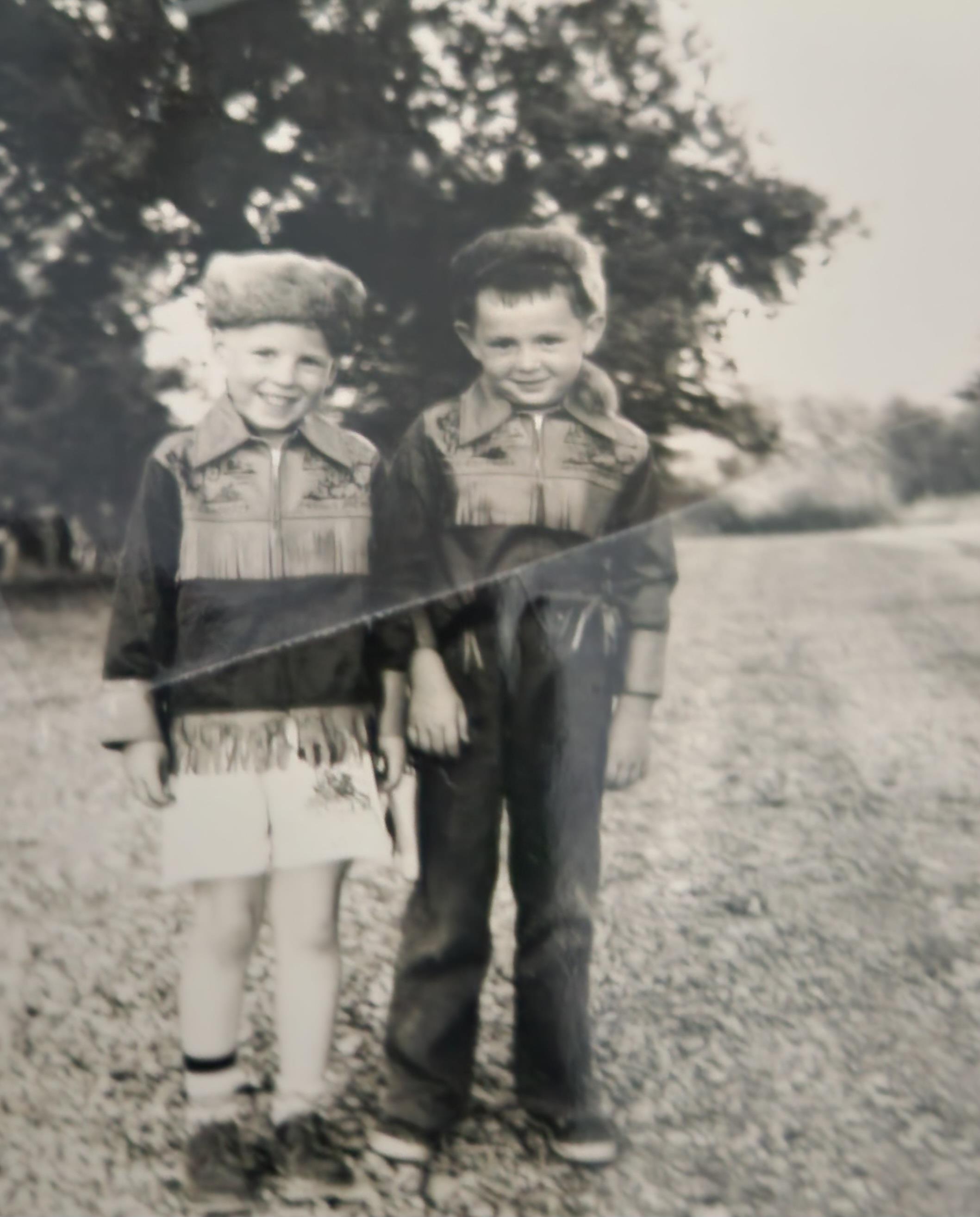Two young boys stand together on a gravel path, smiling in matching jackets.