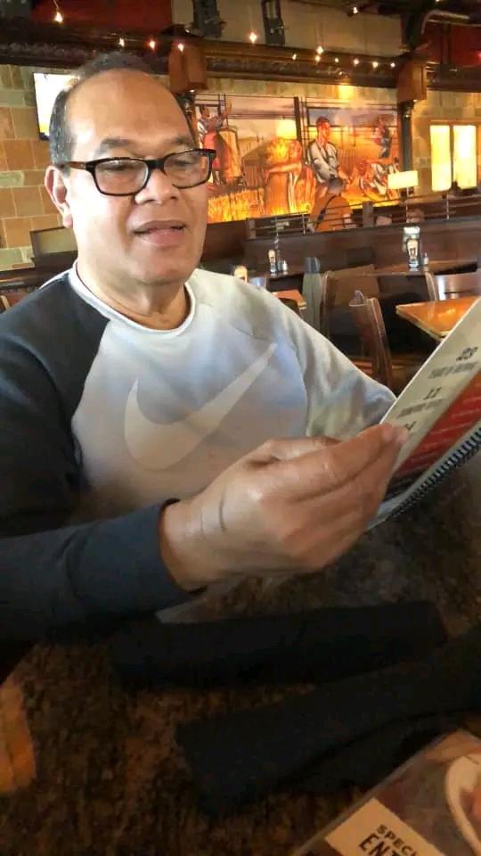 A middle-aged man is looking at a menu while seated at a restaurant table, enjoying his meal.