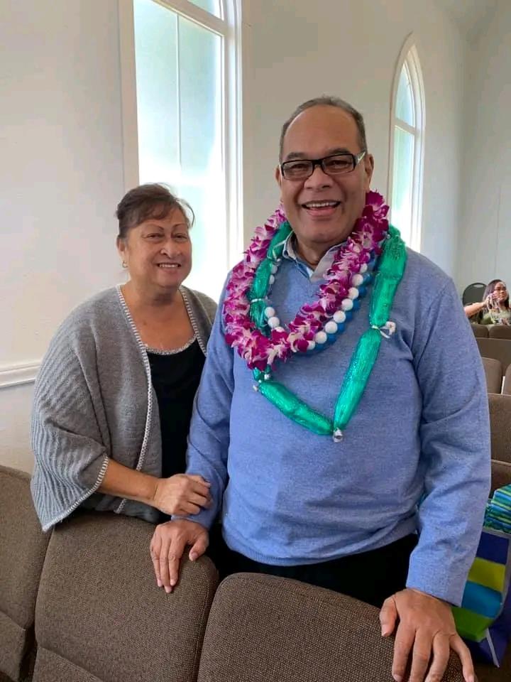 A joyful moment at a gathering featuring two individuals wearing leis, smiling and celebrating.