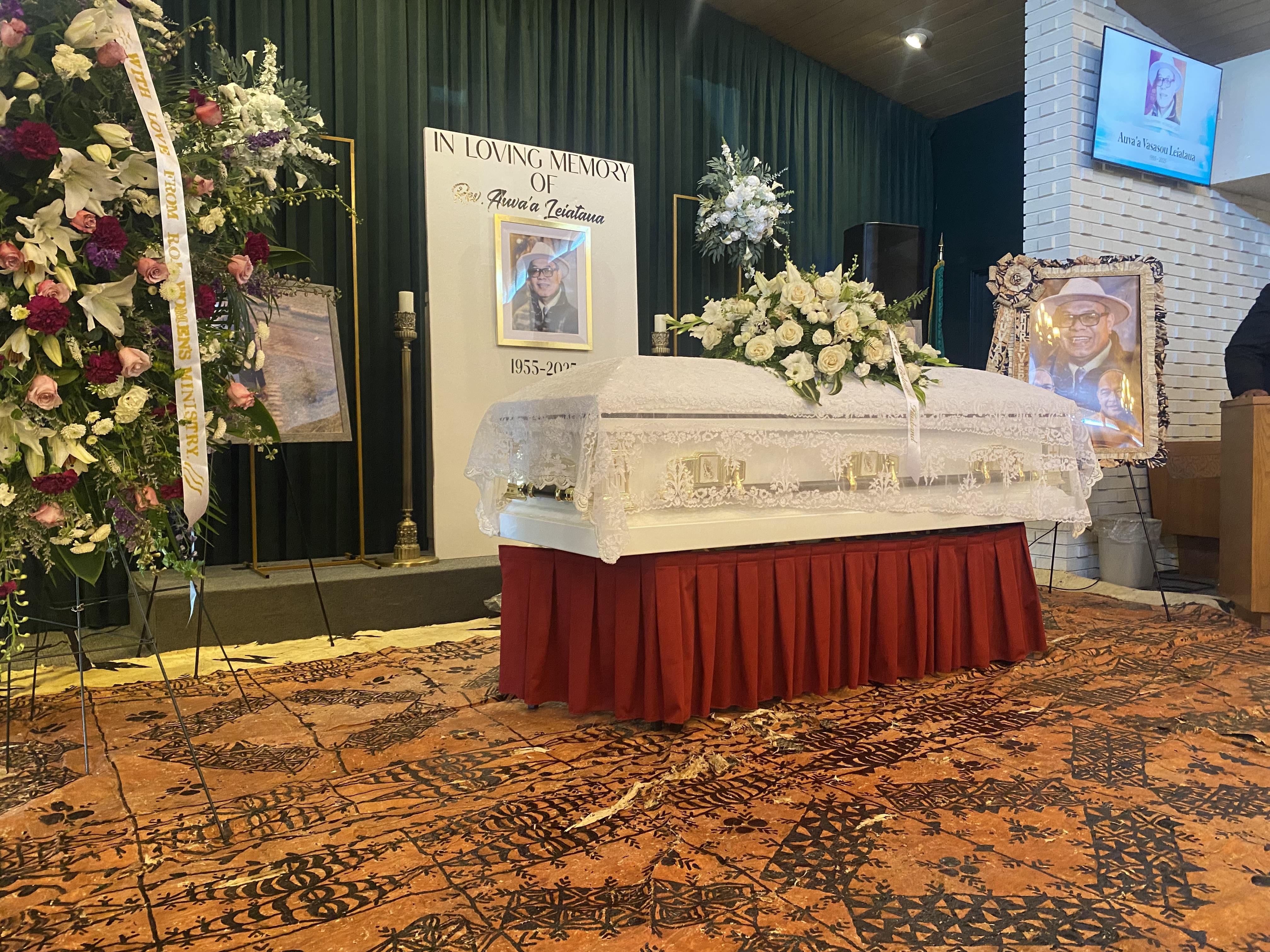 A casket surrounded by floral arrangements and pictures, prepared for a memorial service.