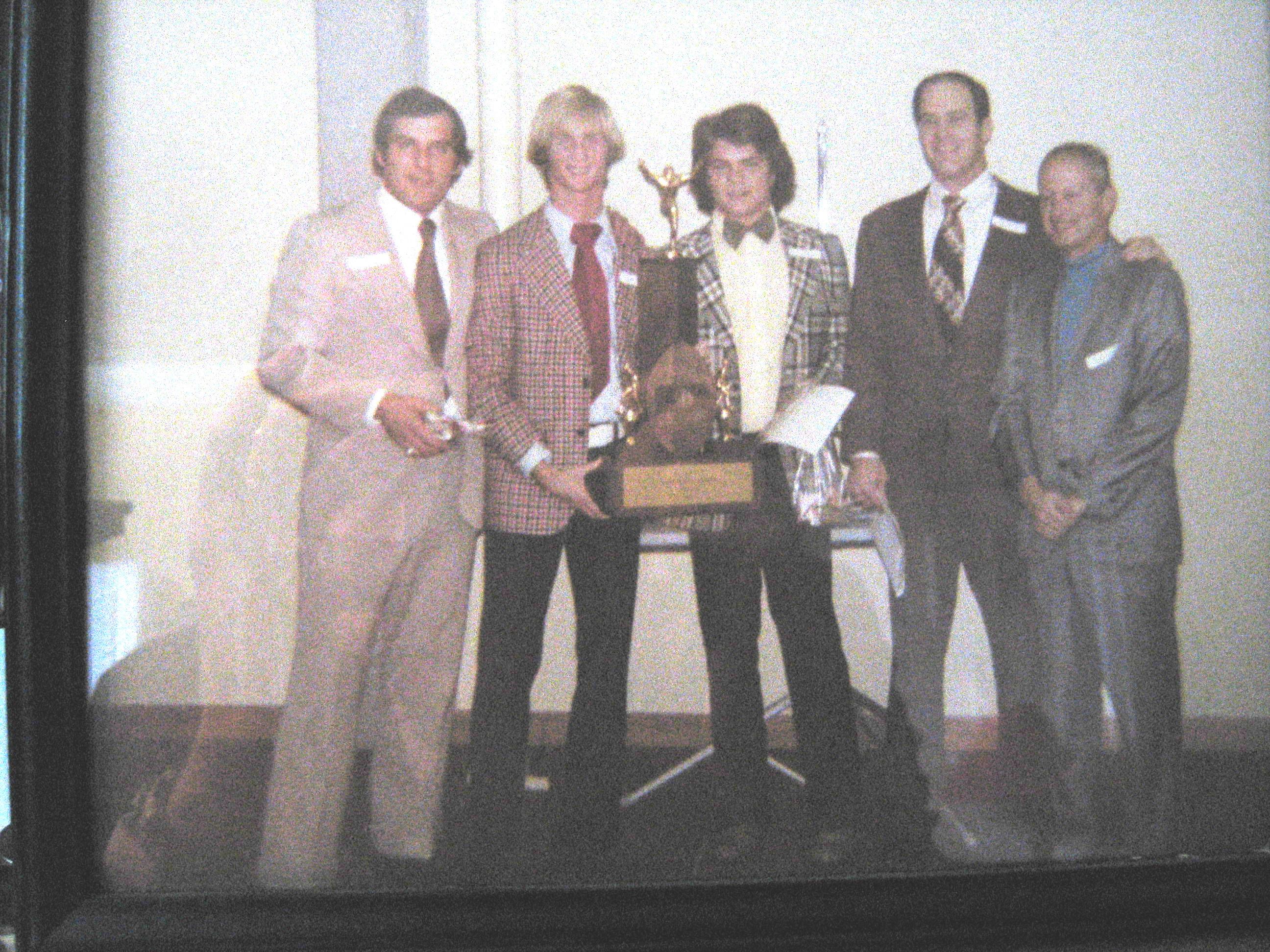 Five men stand together at an awards ceremony, holding trophies and smiling in celebration.