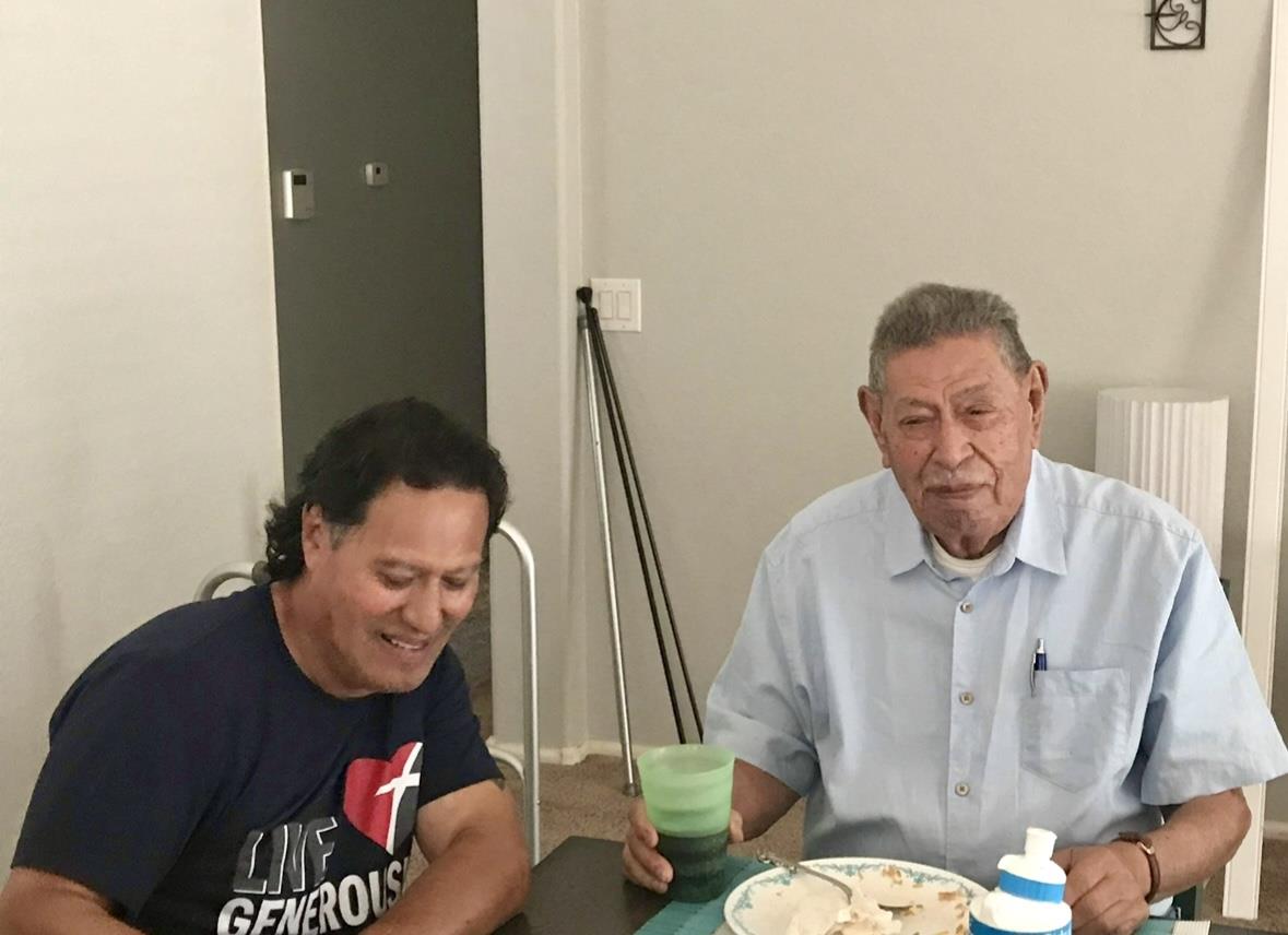 Two men share a moment at the table, surrounded by food and drinks, enjoying each other's company.