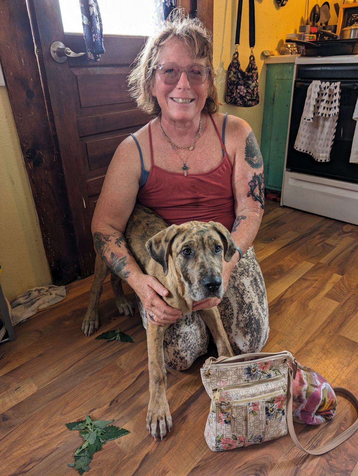 A cheerful woman smiles while sitting on the floor with her dog at home during the day.
