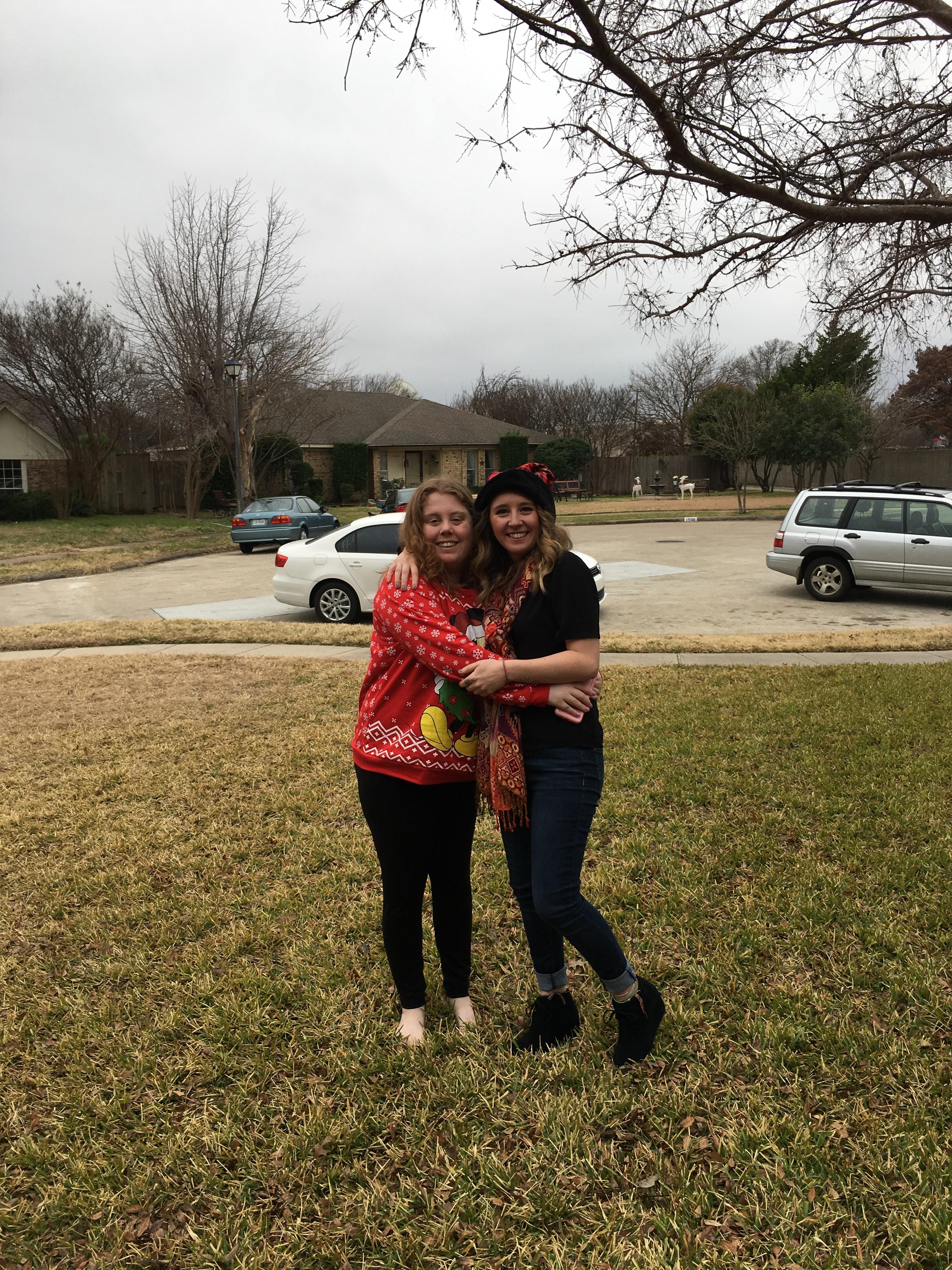Two friends embrace while wearing festive clothing in a yard on a cloudy winter day.