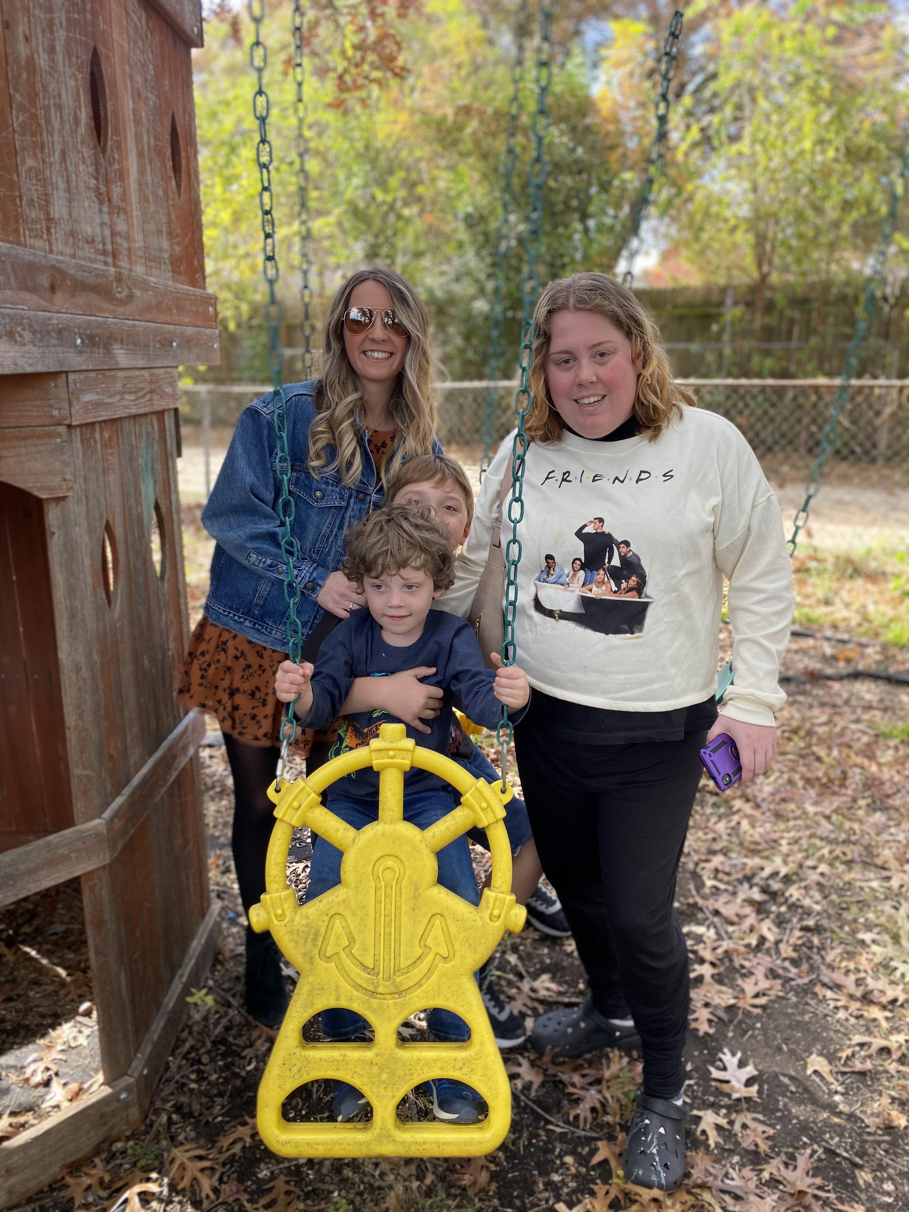 Group of adults and kids enjoying playtime at a playground with swings on a sunny day.