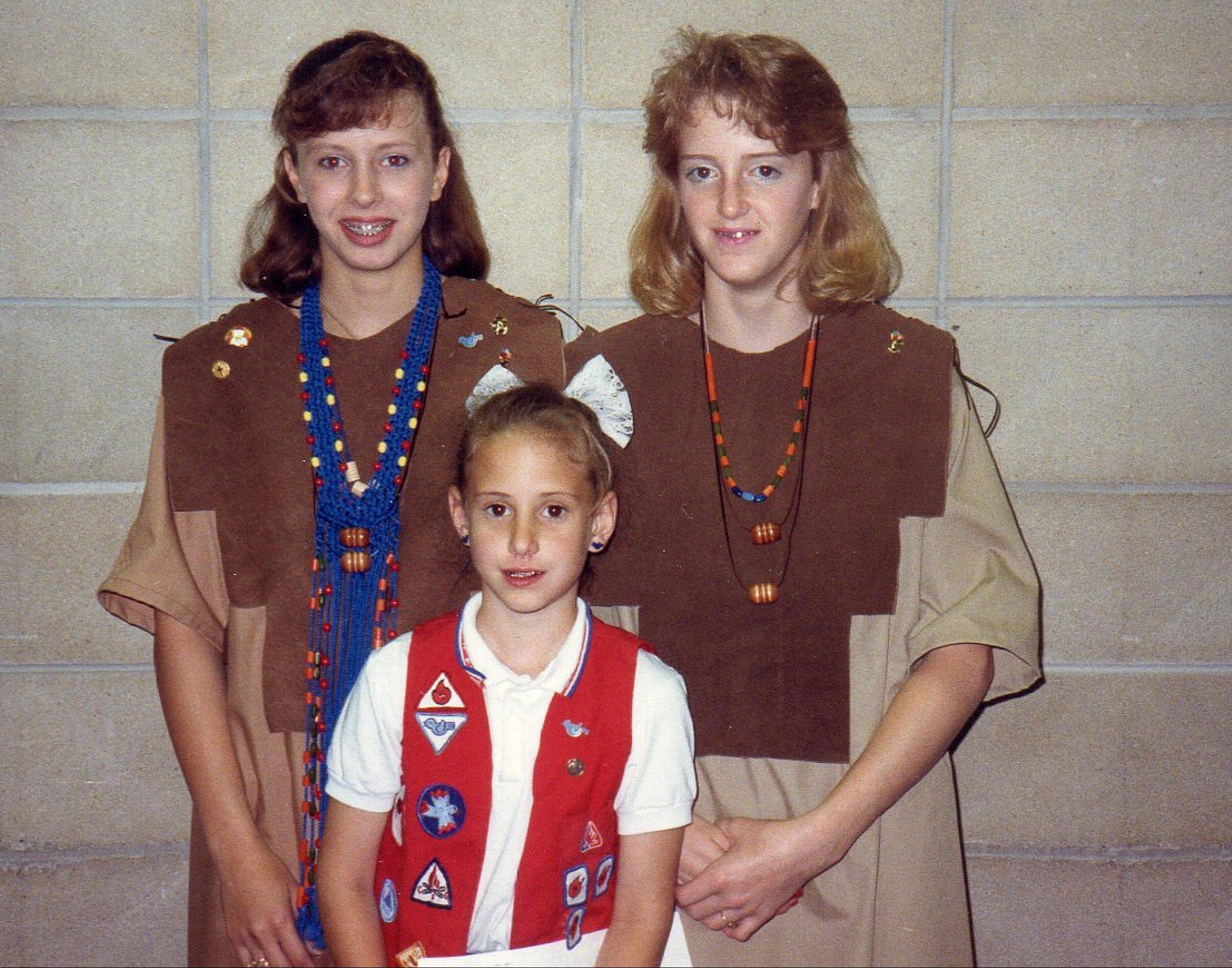 Three girls stand together smiling, showcasing their outfits at a community event indoors.