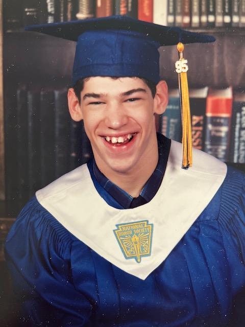 Young man celebrates his graduation wearing a blue cap and gown with a joyful expression.