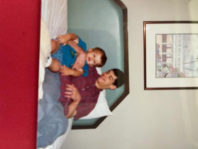 A father shares cherished smiles with his young son on the bed, enjoying their time together.