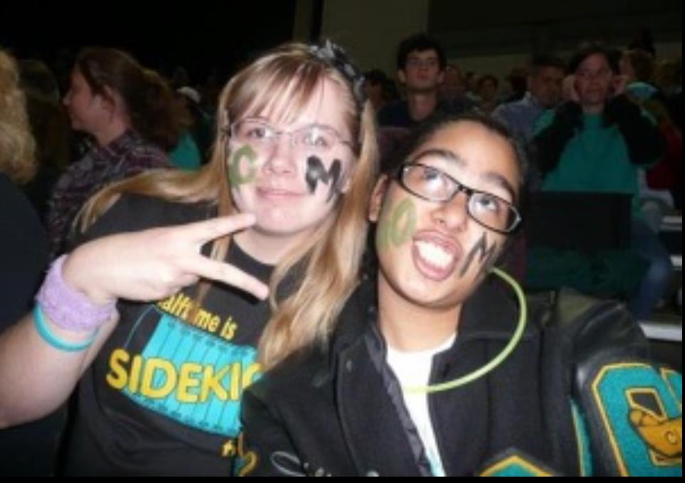 Two students display their school spirit with painted faces and enjoy a lively pep rally atmosphere.
