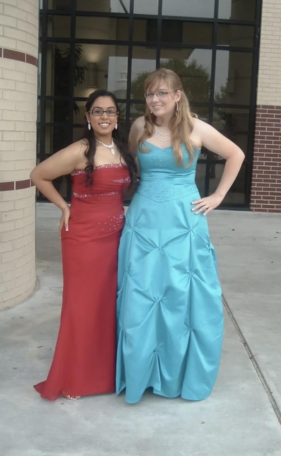 Two friends in colorful gowns confidently pose outside school, smiling brightly.