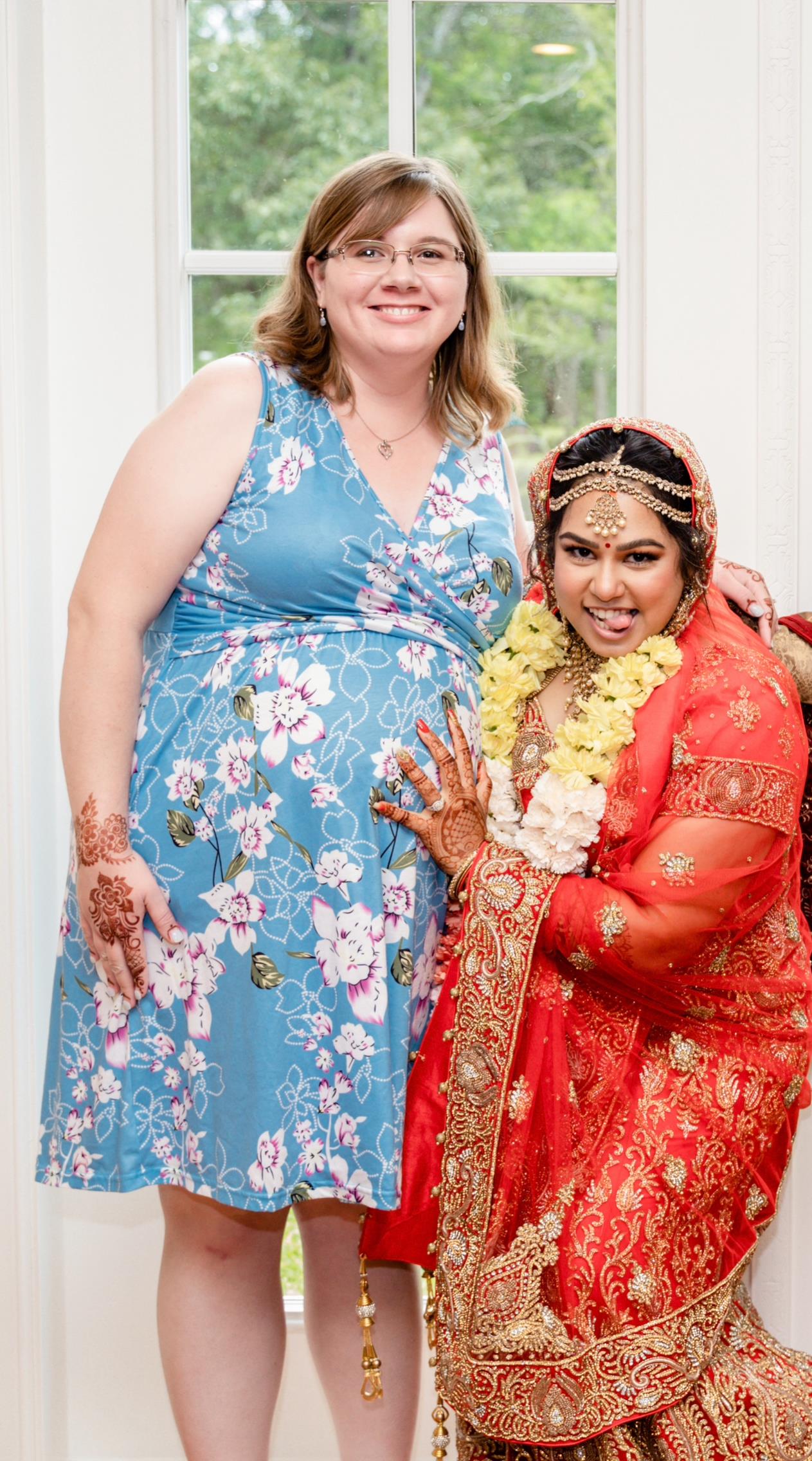 Two women joyfully pose in colorful cultural attire at a lively celebration.