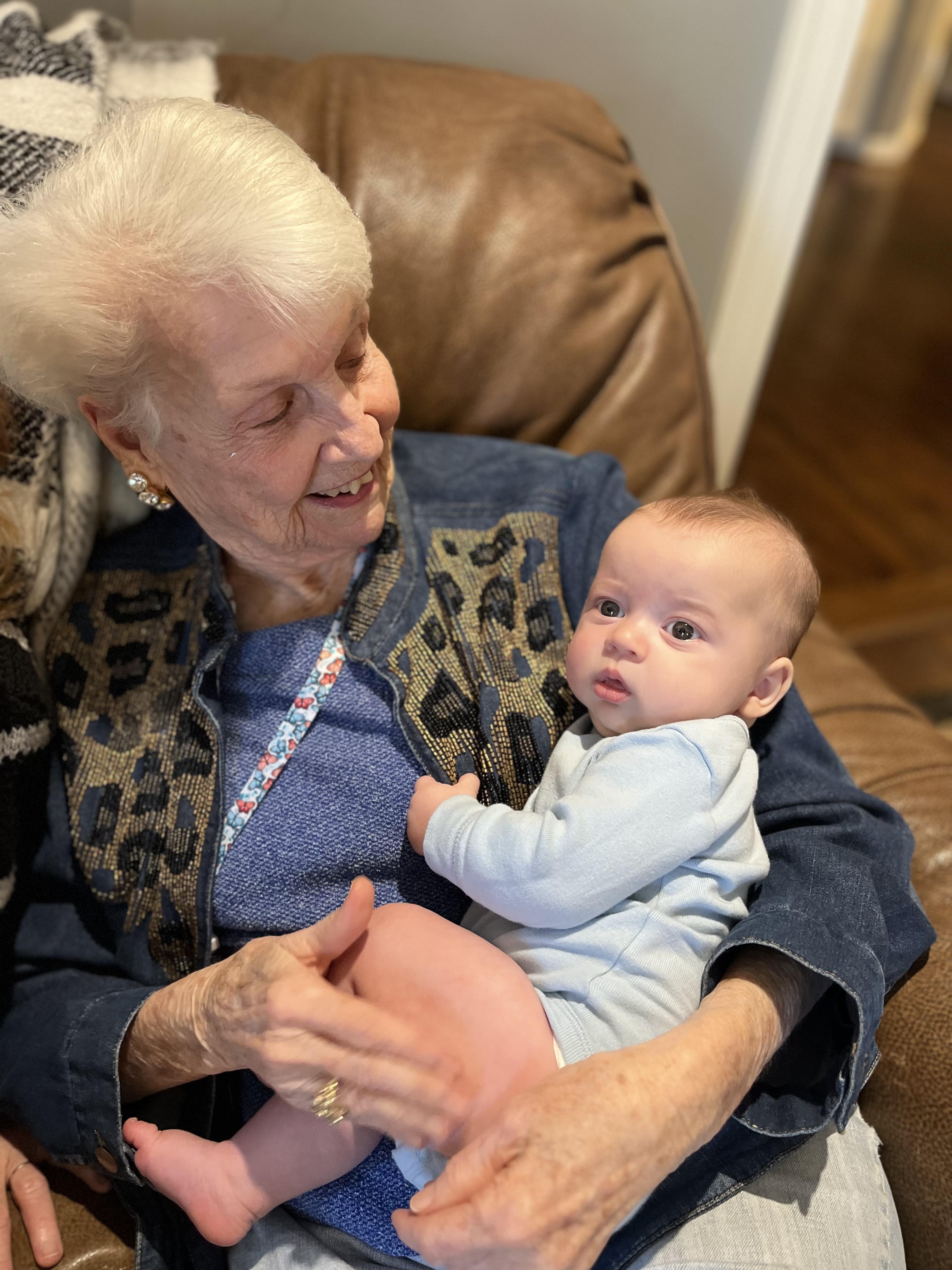 Smiling elderly woman holds her grandchild in a cozy living room, sharing a joyful moment.