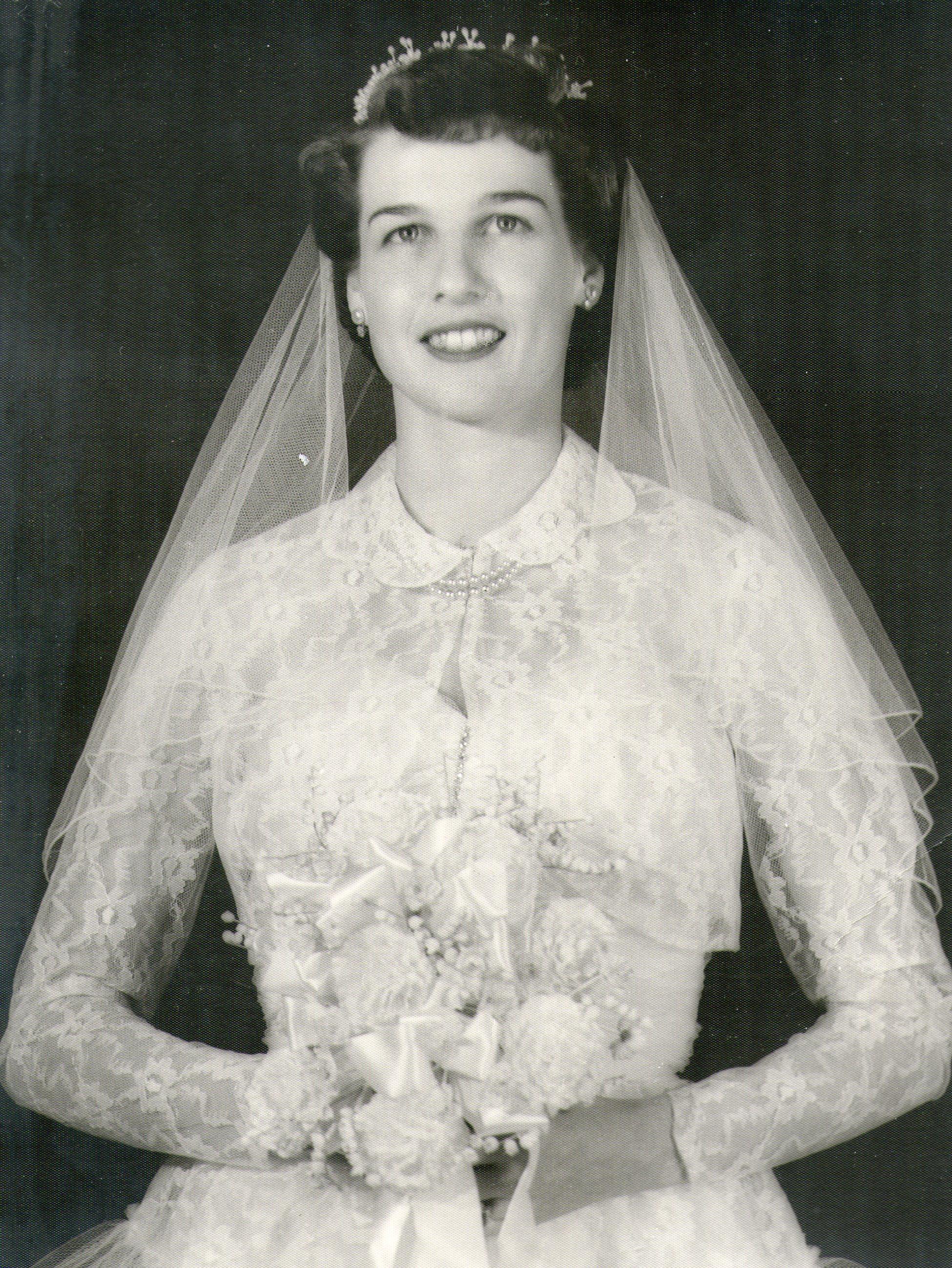 Bride stands proudly holding a bouquet in an elegant lace wedding dress and veil, smiling warmly.