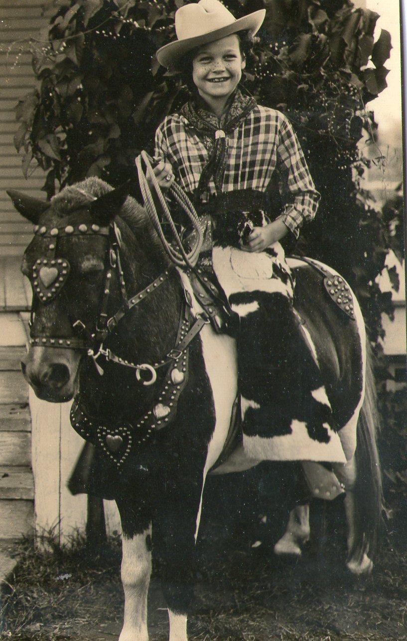 Cowgirl on a adorned horse holds a small dog, showcasing western attire and playful spirit.