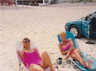 Two women in swimsuits enjoy their time lounging on beach chairs, soaking up the sun.