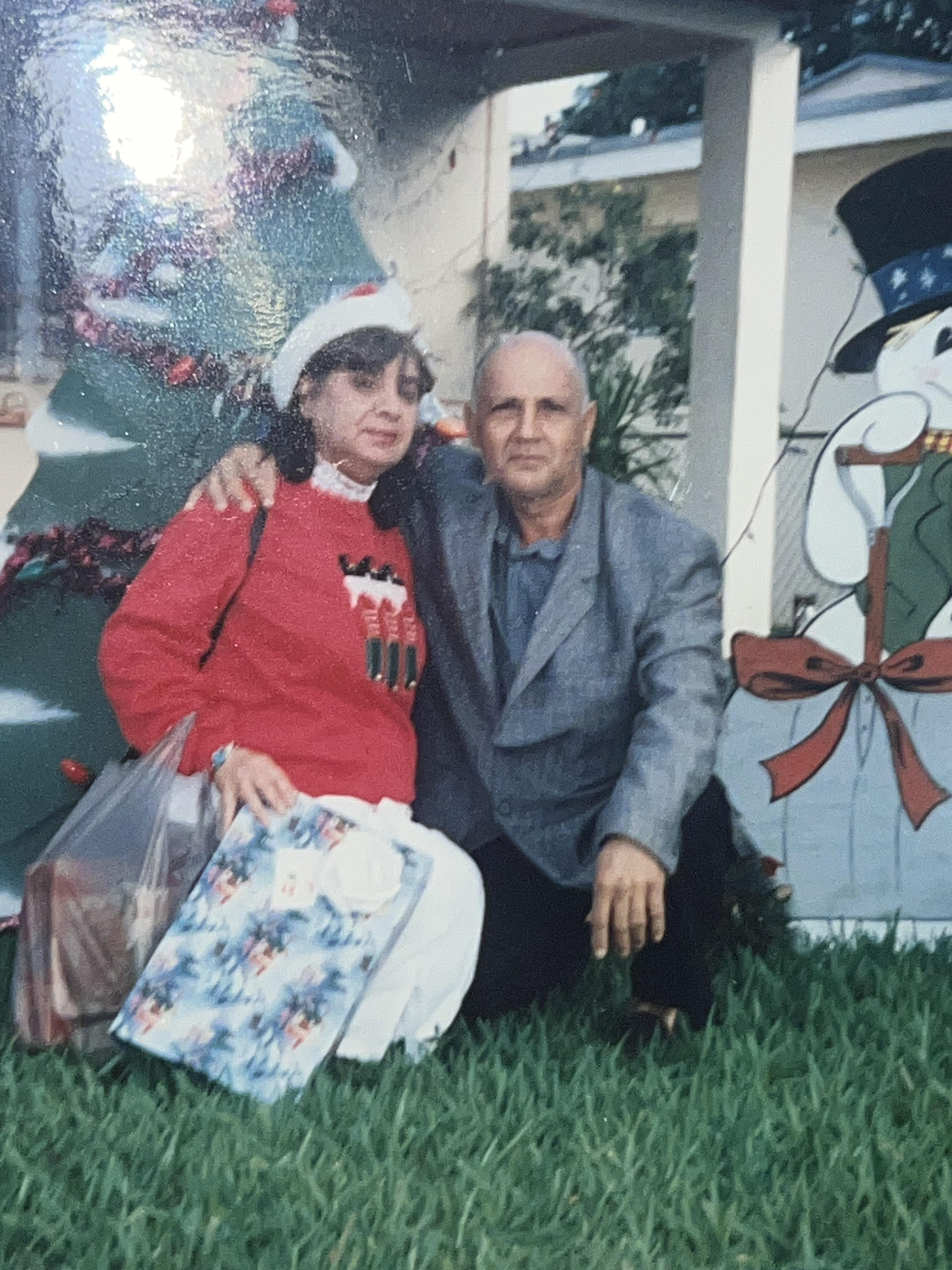 Couple wearing bright clothes poses joyfully next to holiday decorations outdoors in a neighborhood.