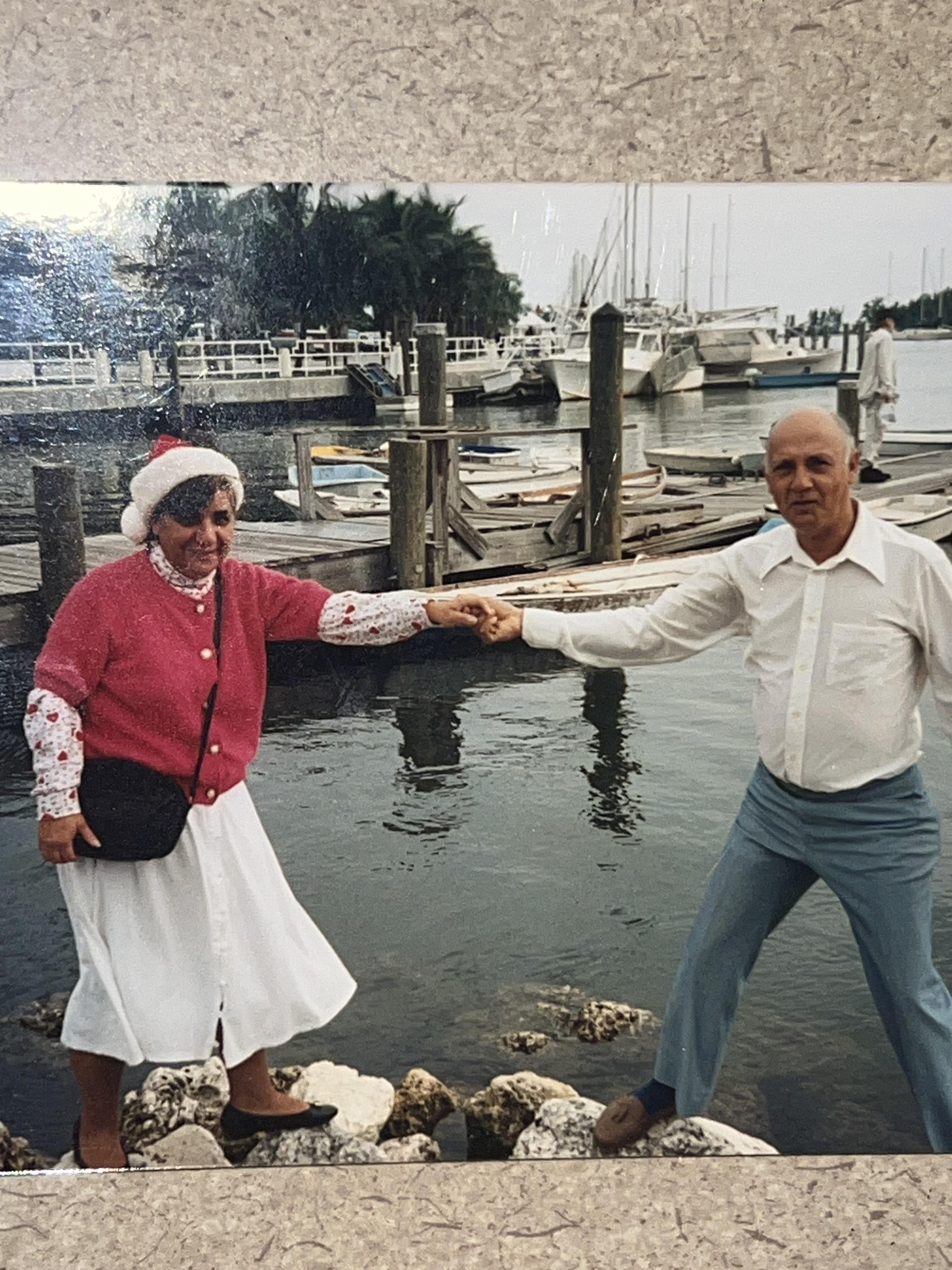 Two seniors dance happily by the water, surrounded by boats and a charming marina.
