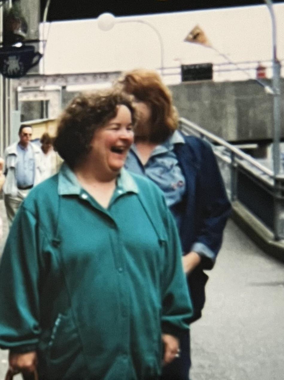 Two women share a moment of laughter while walking down a bustling street in a city.