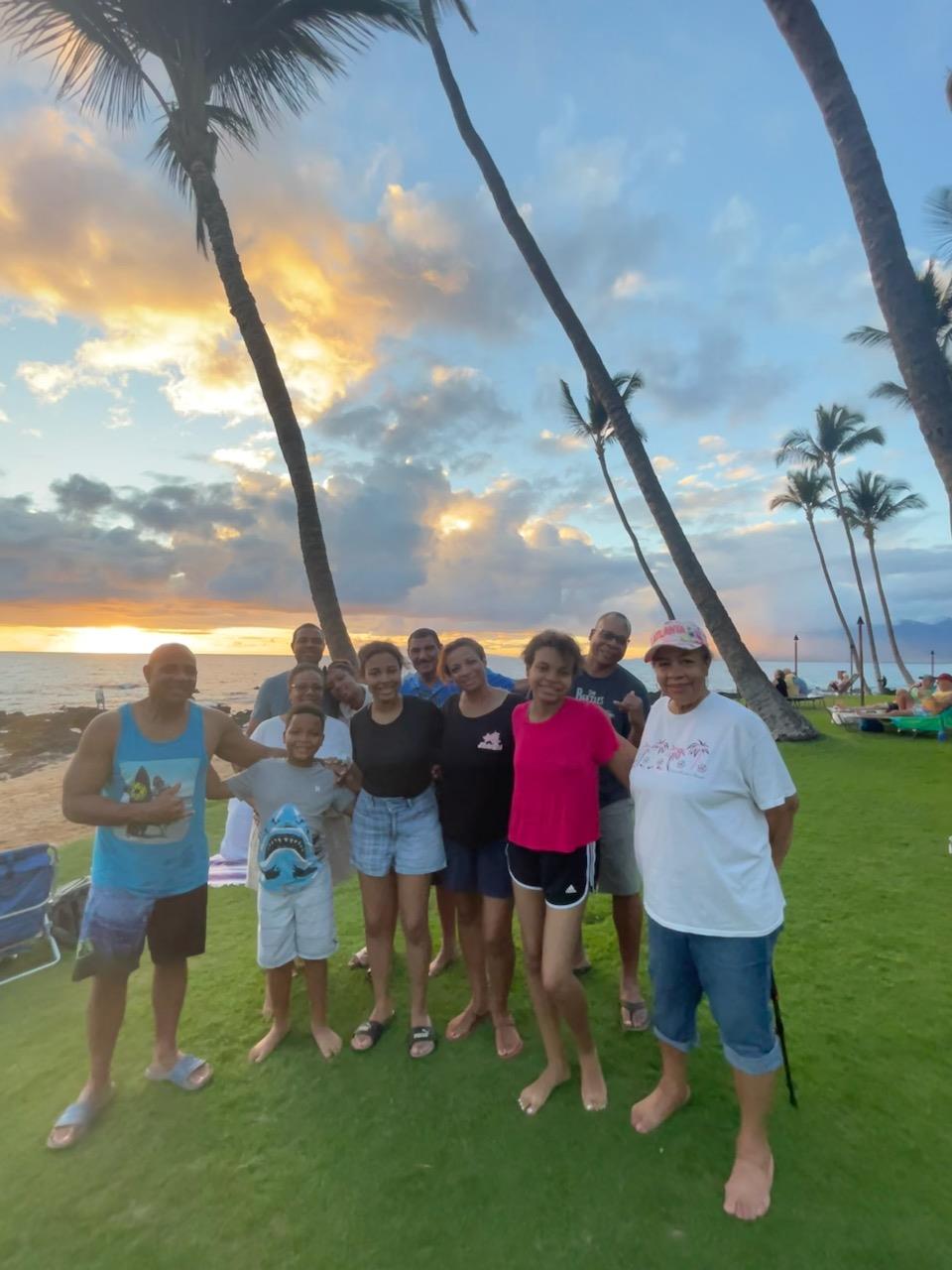 Group of friends and family enjoy a beach gathering during sunset, surrounded by palm trees.