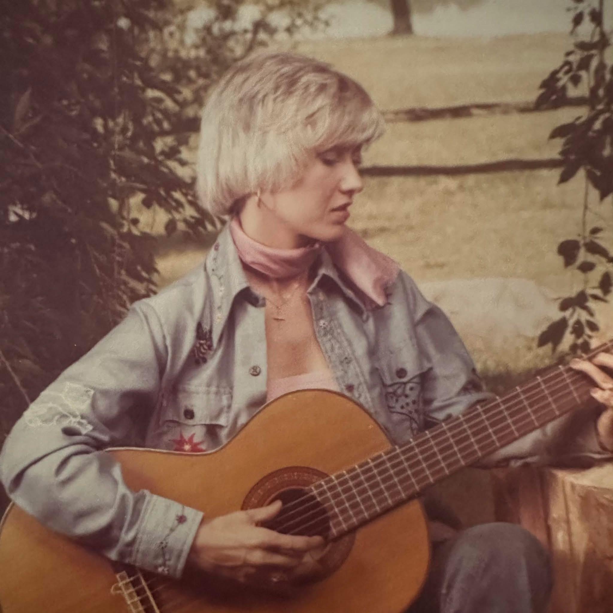 Female musician strums her guitar while enjoying a peaceful moment in a natural setting.