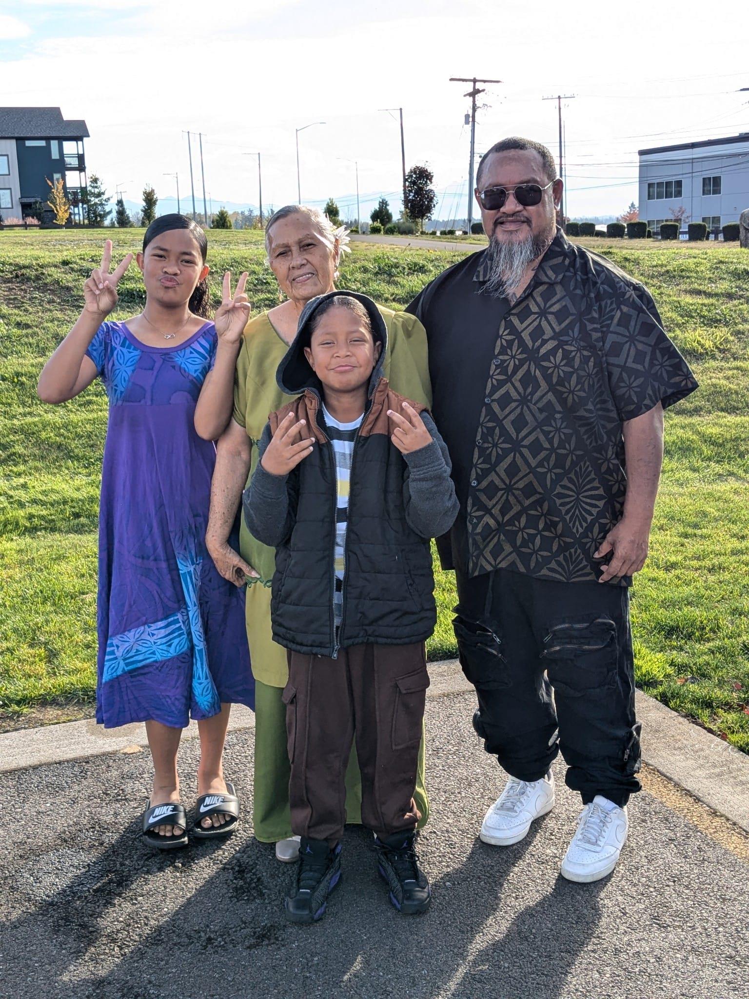 Four family members enjoy a cheerful moment together in the park, sharing smiles and peace signs.