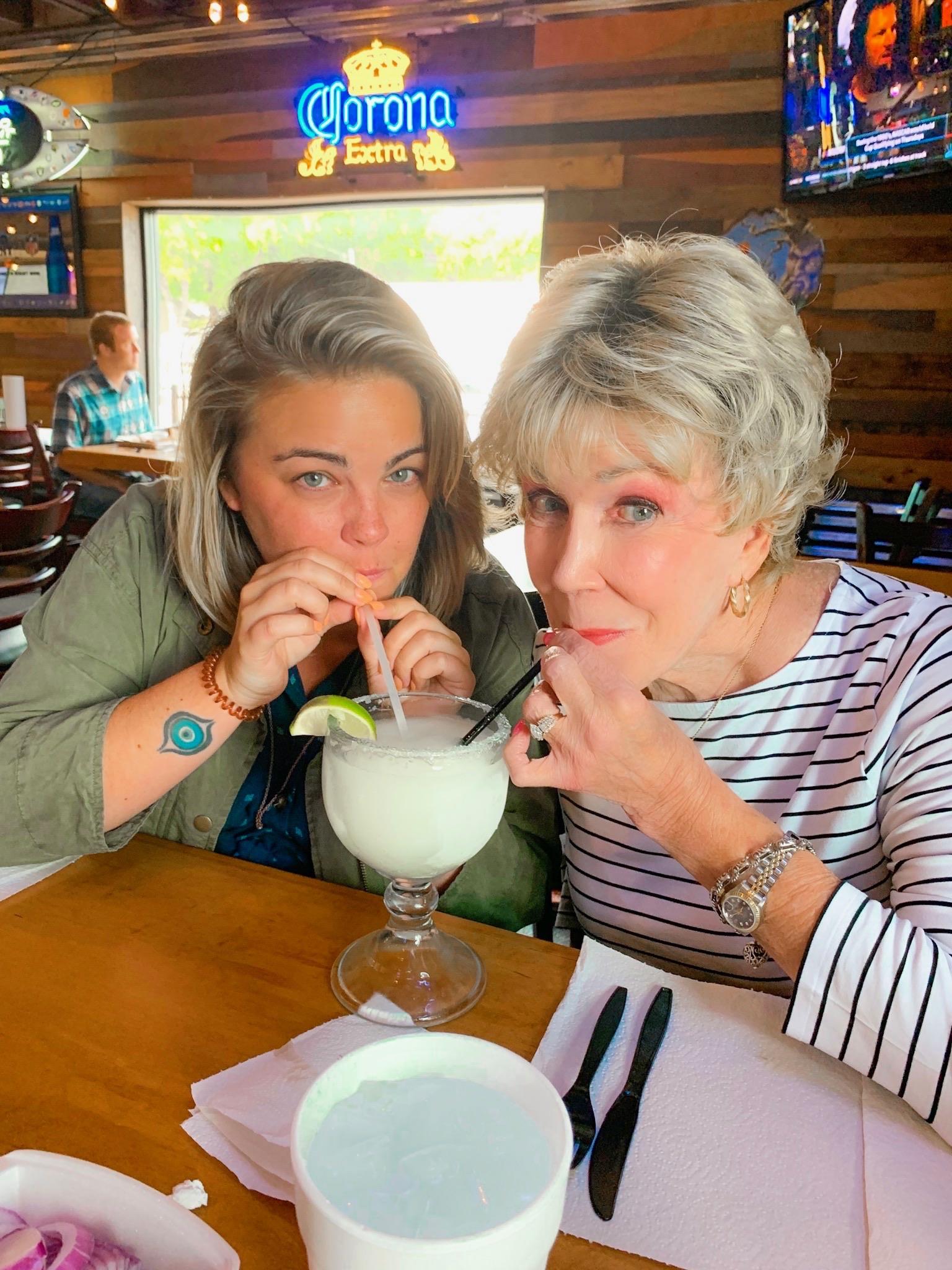 Two women smile and enjoy a refreshing drink at a busy restaurant.