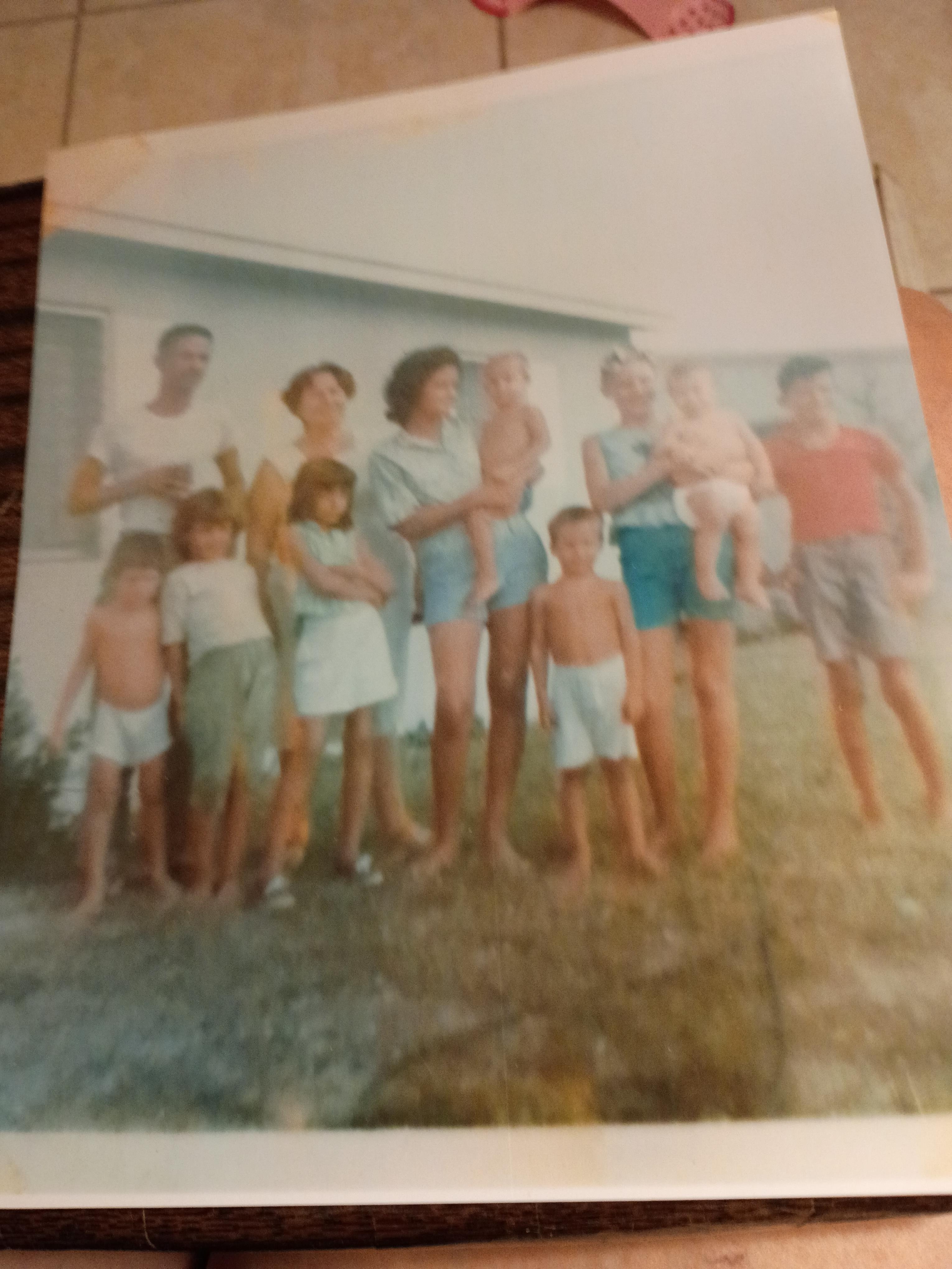 A large group of children and adults are gathered outside a house, enjoying a bright day.