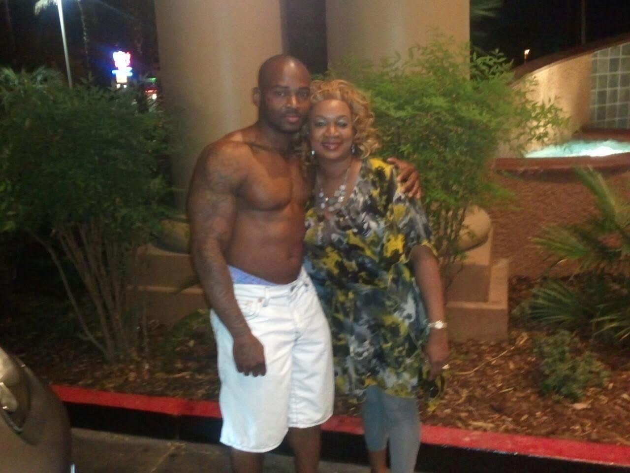 A happy couple stands closely together at night, surrounded by plants and urban lights.