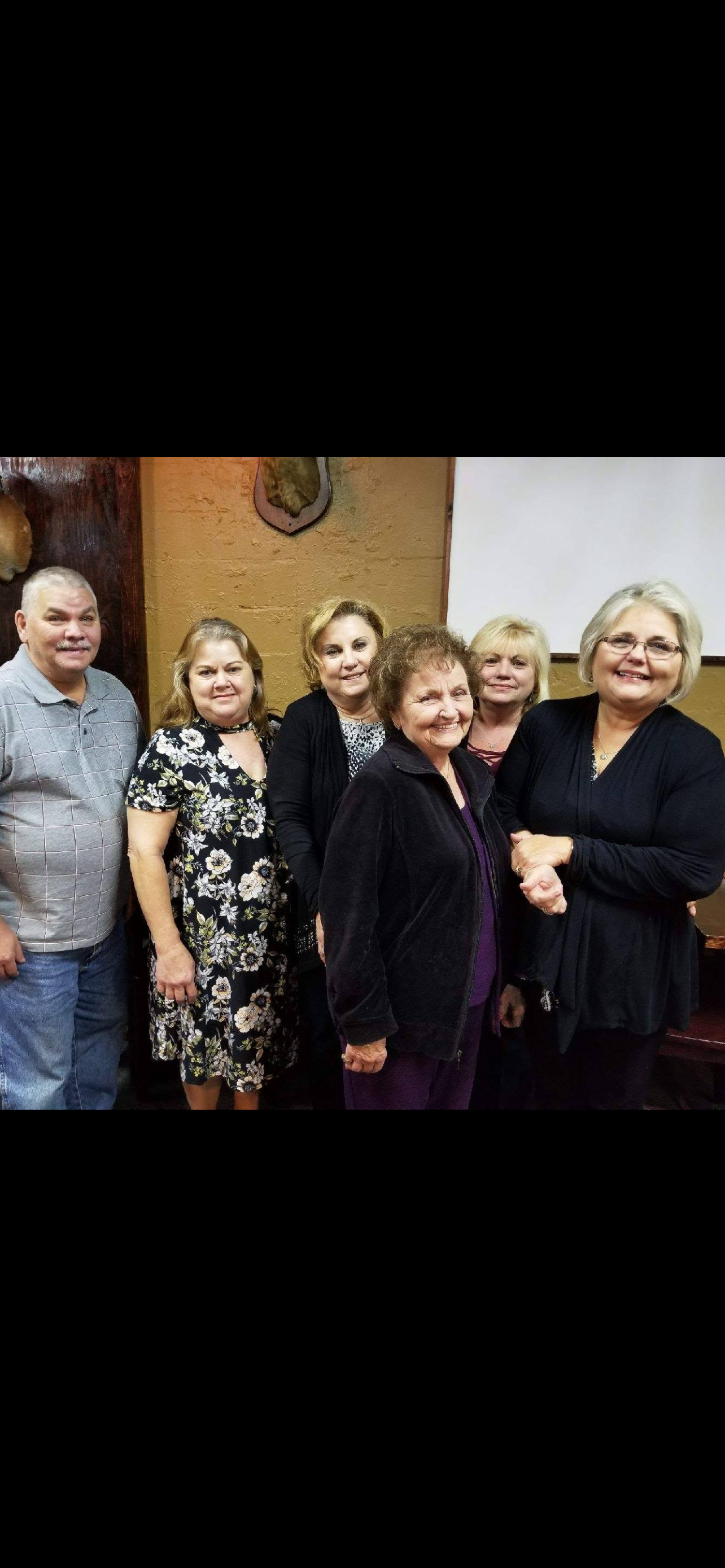 Six family members stand together, smiling and sharing a joyful moment in a cozy venue.
