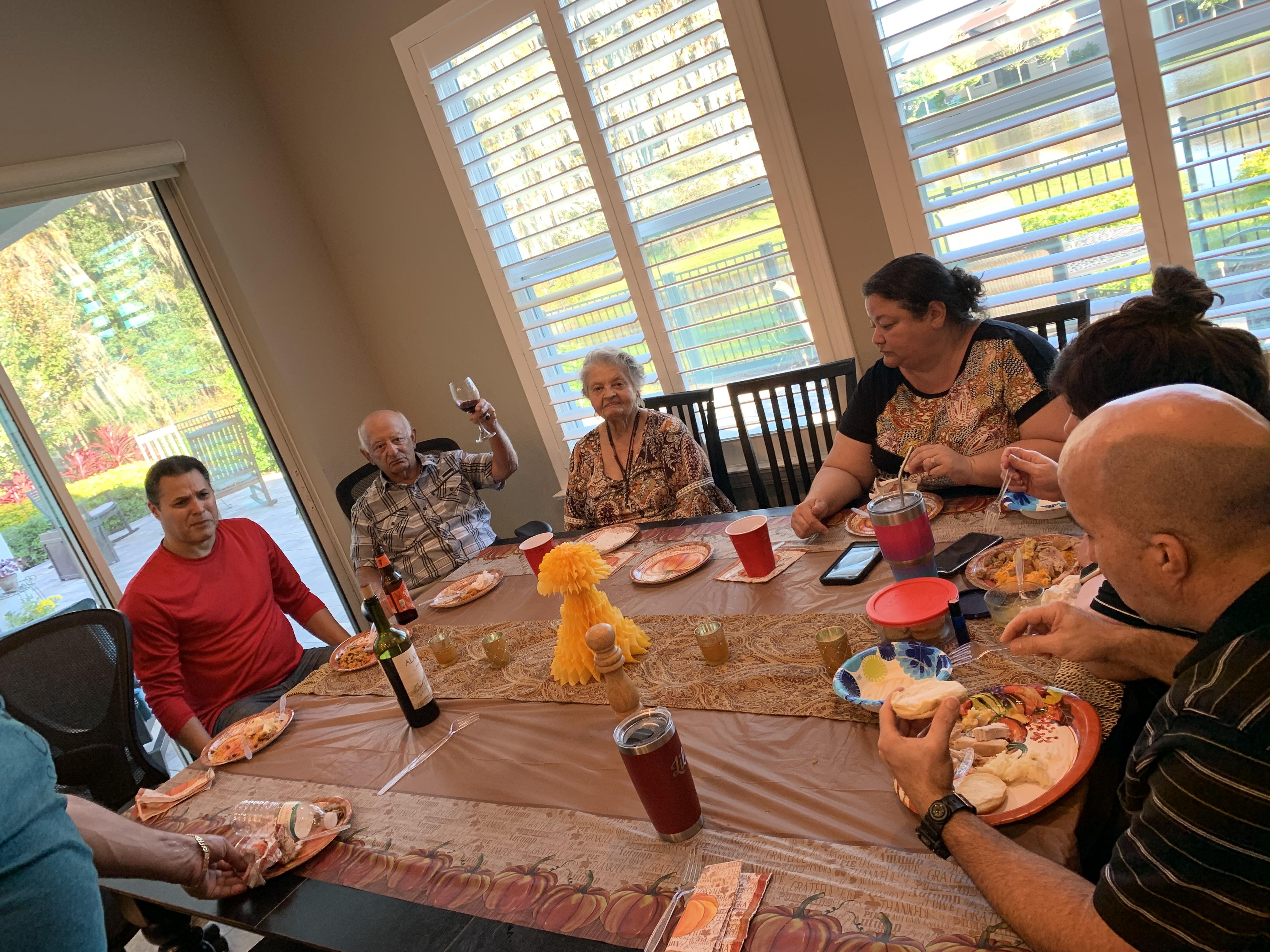 Family gathers around a large table, laughing and enjoying food together.