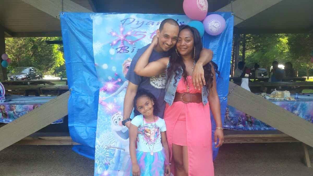 A joyful family stands together at a birthday party, surrounded by bright decor and balloons.
