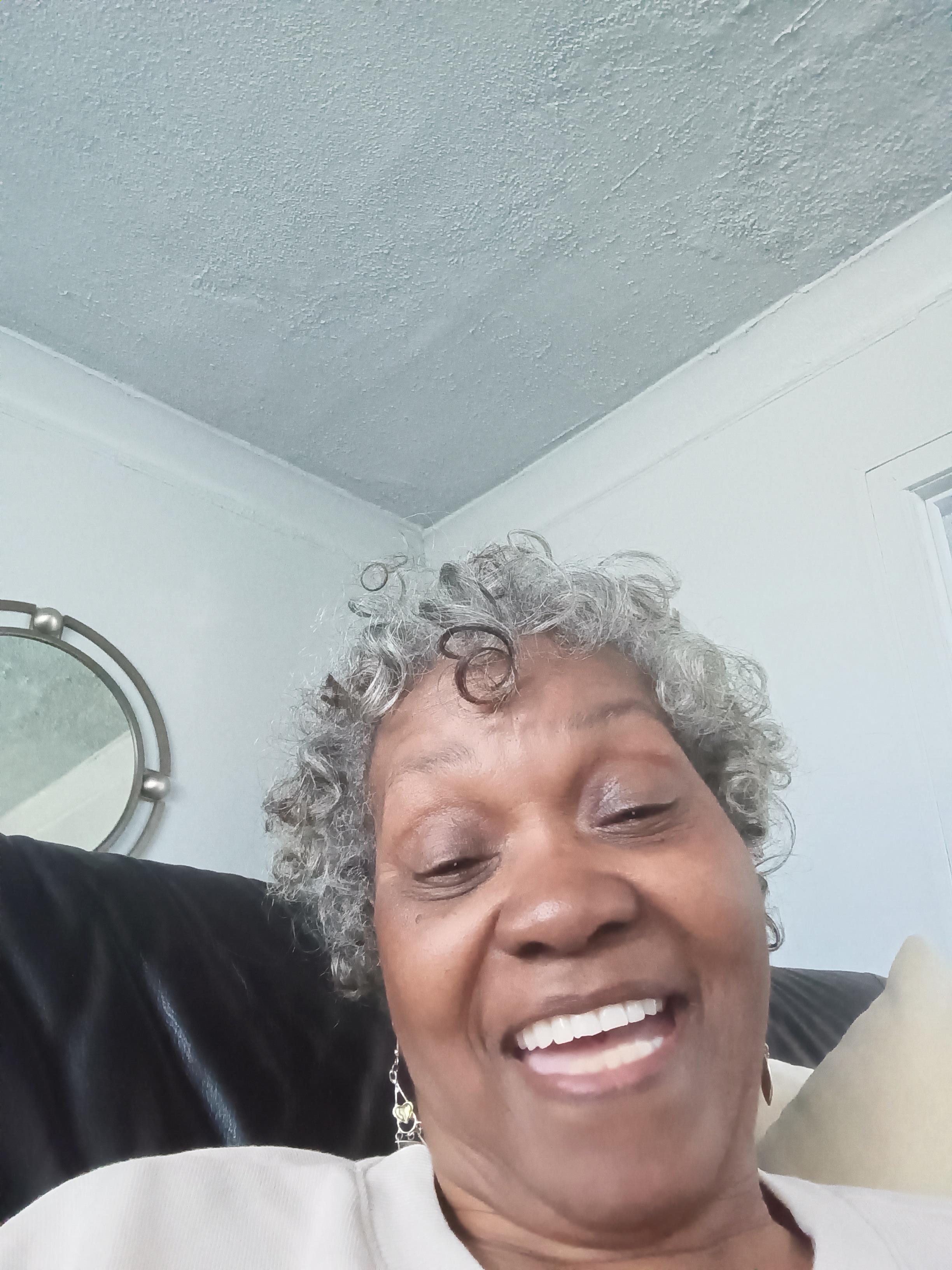 An elderly woman smiles warmly in her cozy living room, radiating joy.