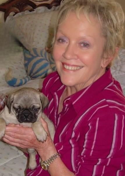 A joyful woman enjoys her time with a small pug puppy, sharing a moment of warmth at home.