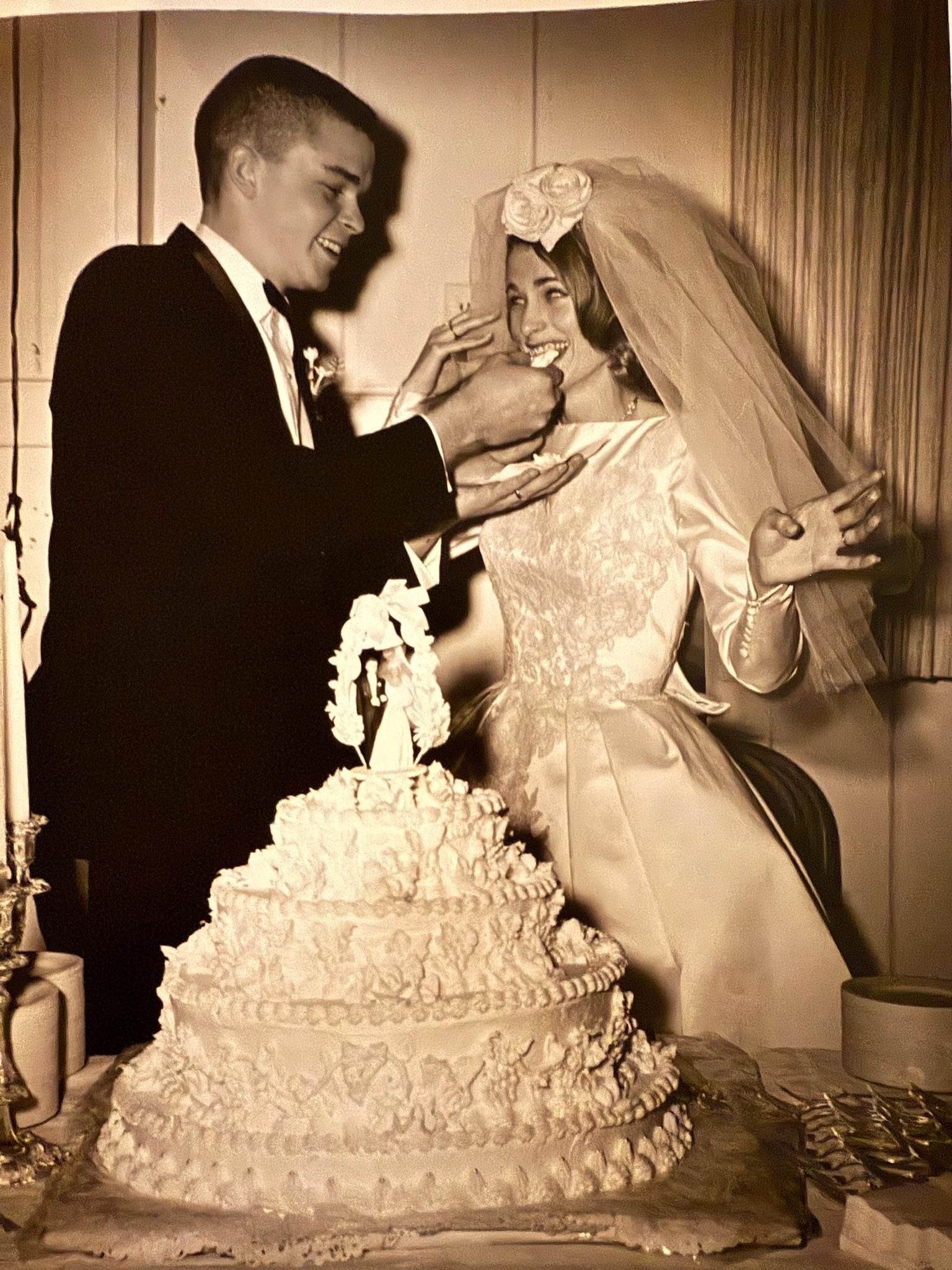 Newlyweds joyfully feed each other cake while surrounded by festive decorations and candlelight.