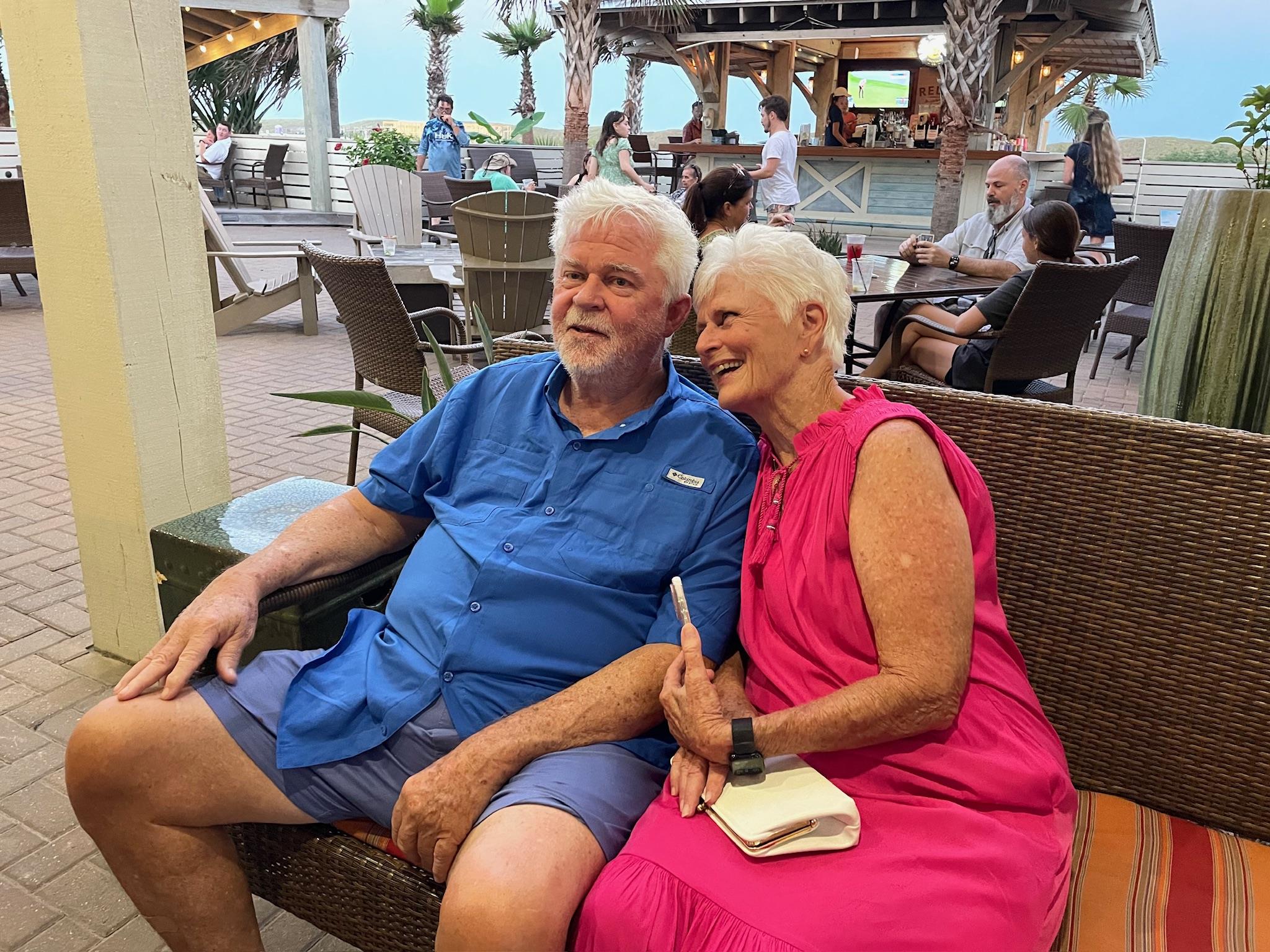 Older couple relaxes in comfortable chairs, sharing a moment of joy at a beachfront cafe.