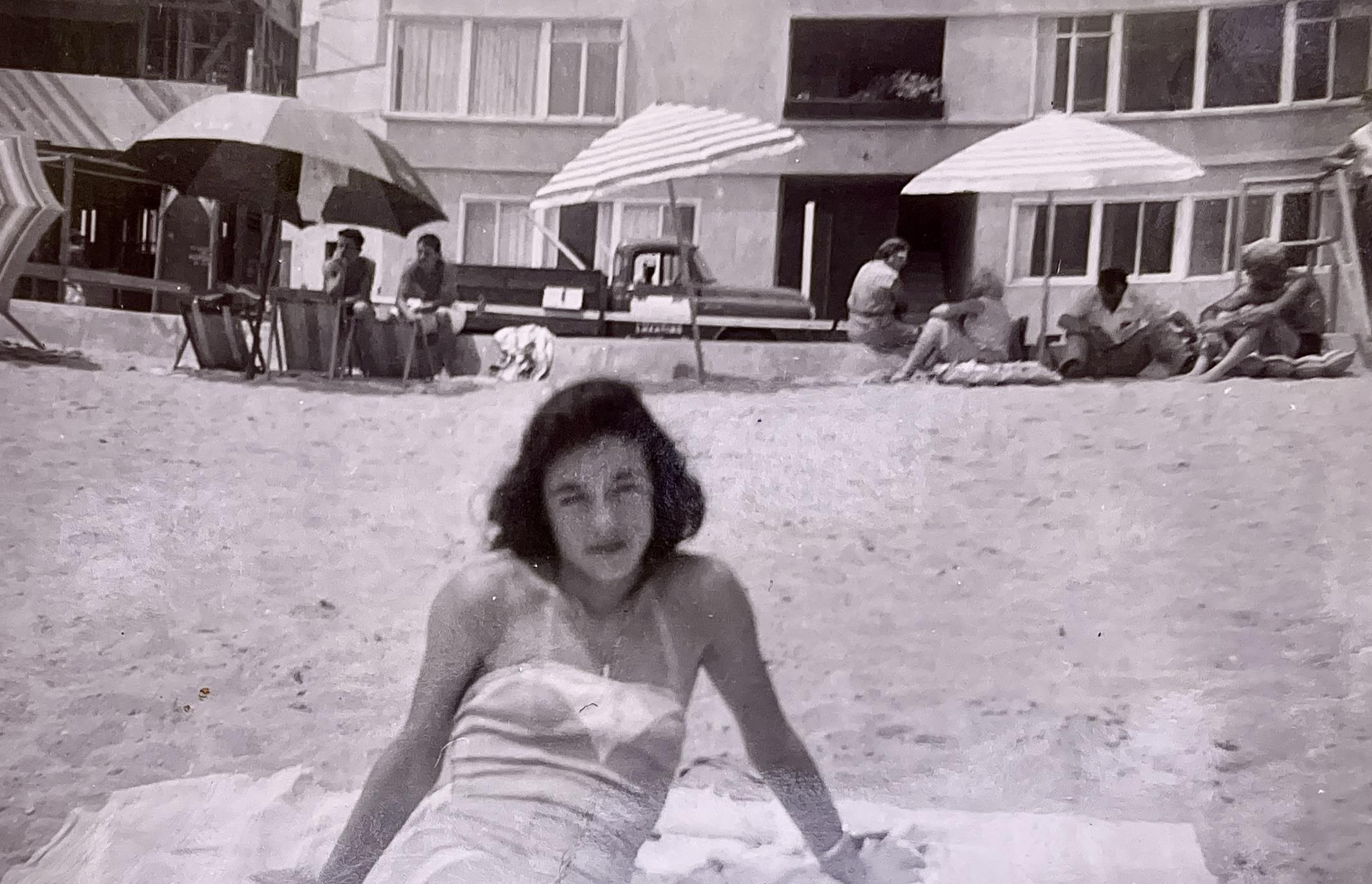Woman enjoying a sunny day at the beach while others gather around her in the sand.