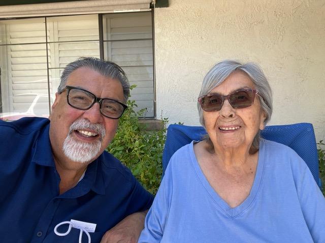 Two seniors sit happily in outdoor chairs, enjoying a sunny day and each other's company.