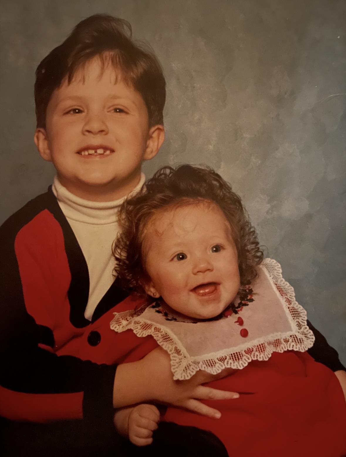 Two children smile happily while posing in matching outfits against a soft backdrop.