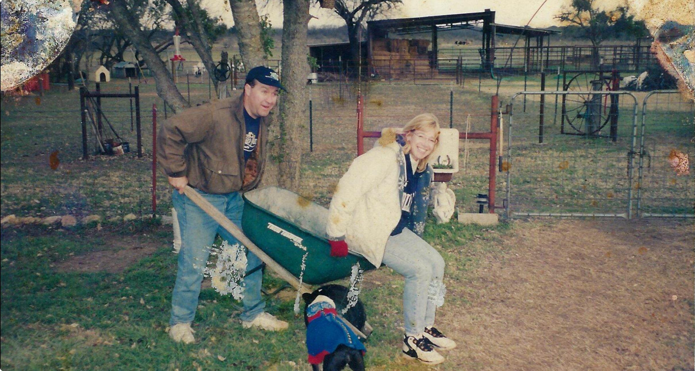 Two friends enjoy transporting one pal in a wheelbarrow on a playful farm.